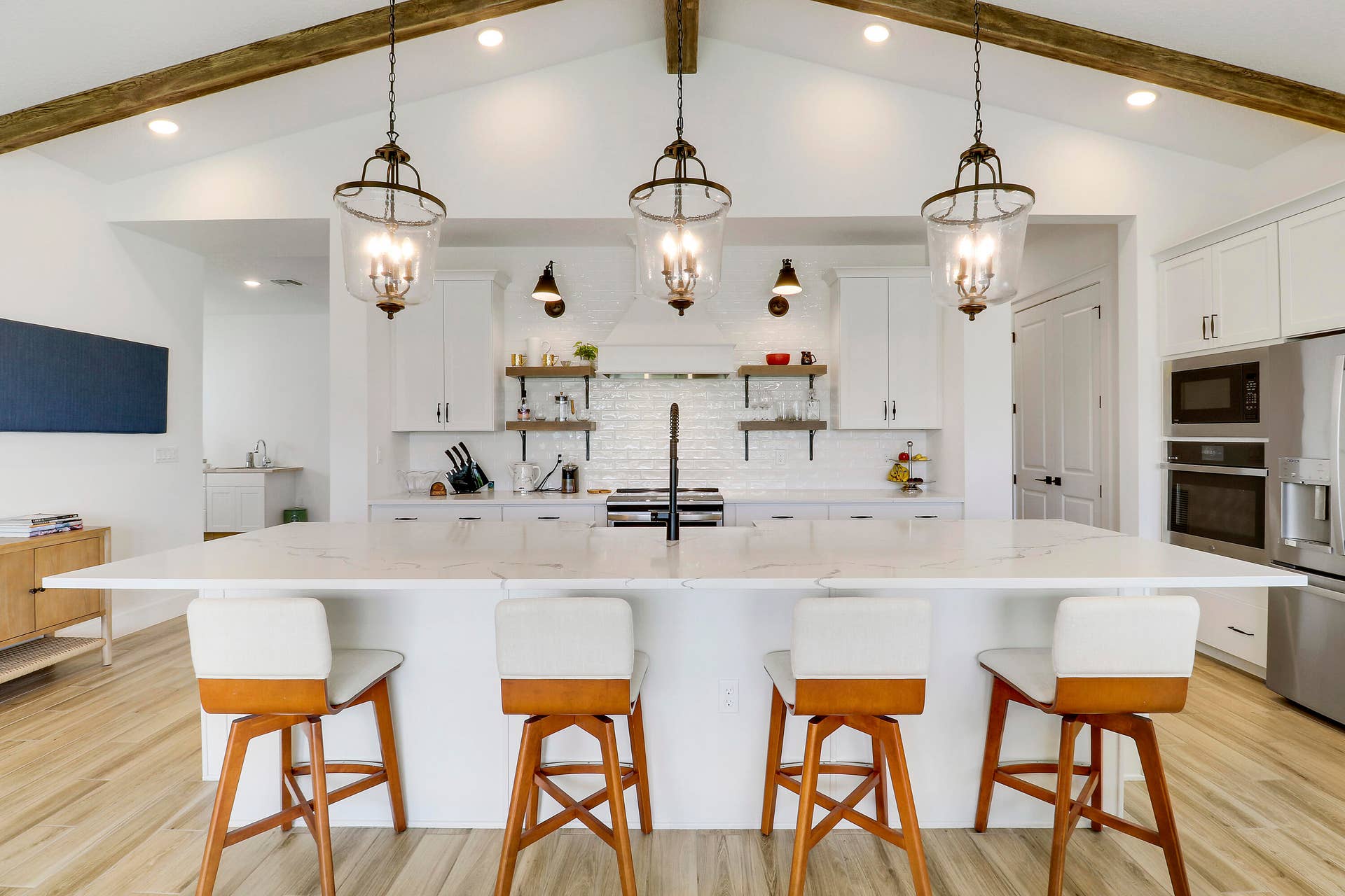 6742 SE LOST PINE Drive, Stuart, FL 34997 Kitchen featuring a central island with a stone-finish countertop, vaulted ceiling with exposed wood-finish like beams, white cabinetry, lantern-style pendant lighting, and subway tile backsplash