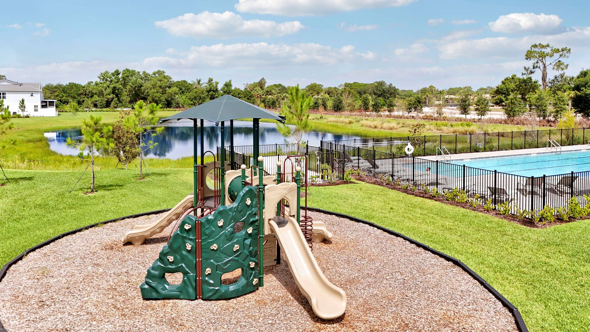 6742 SE LOST PINE Drive, Stuart, FL 34997 Outdoor recreation area featuring a playground with slides and a climbing wall, a fenced swimming pool, and a water feature surrounded by landscaping.