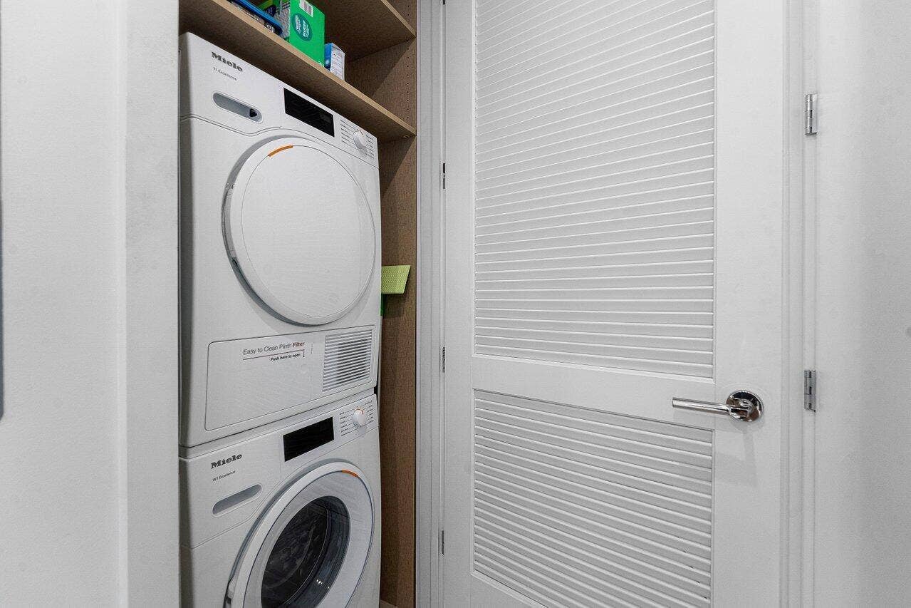 Built-in stacked Miele laundry appliances, louvered white door, and integrated shelving