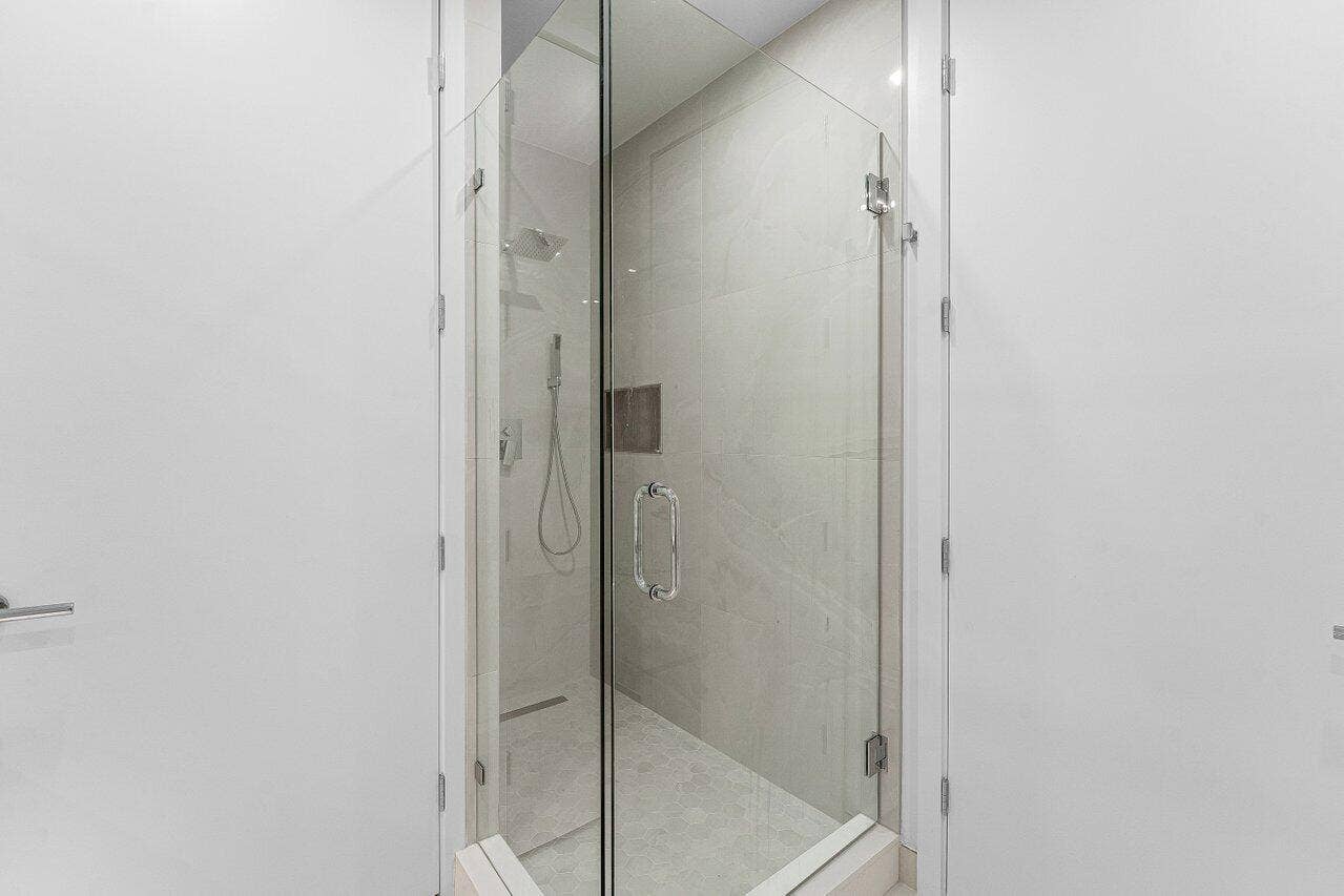 Walk-in shower featuring a glass enclosure with polished hardware, oversized wall tile, rainfall showerhead, and wall-mounted hand shower