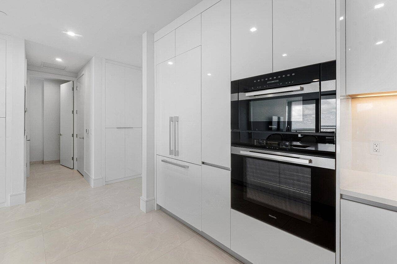 Kitchen featuring floor-to-ceiling high-gloss white cabinetry, integrated stainless steel appliances, a built-in wall oven, and light-toned tile flooring