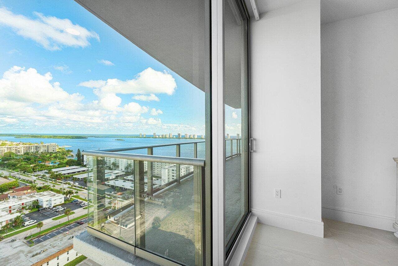 Full-height sliding glass doors opening to a glass-paneled balcony overlooking the water