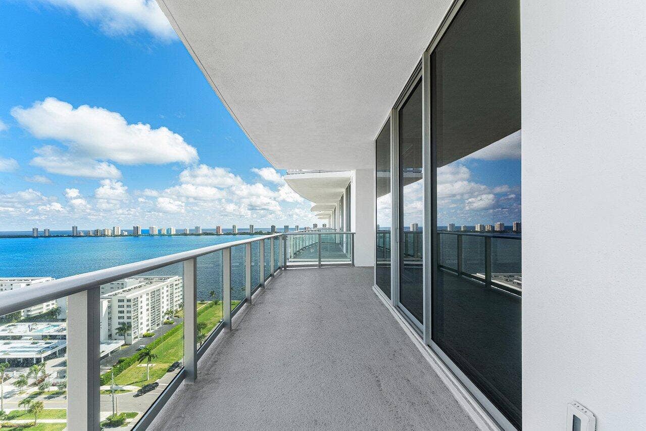 Expansive covered balcony featuring glass panel railings, floor-to-ceiling sliding glass doors, and concrete flooring