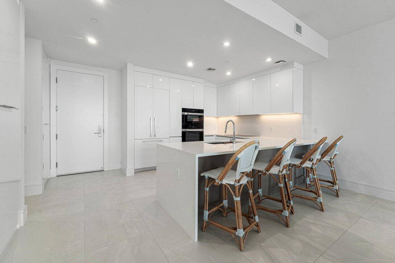 Contemporary kitchen featuring high-gloss cabinetry, stone-surface countertops, a waterfall-edge island with seating, built-in stainless steel appliances, and large-format tile flooring