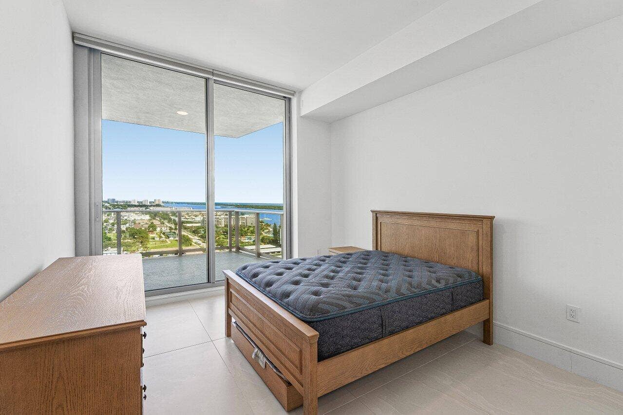 Floor-to-ceiling sliding glass doors, private balcony with metal railing, light-colored tile flooring, and neutral wall finishes