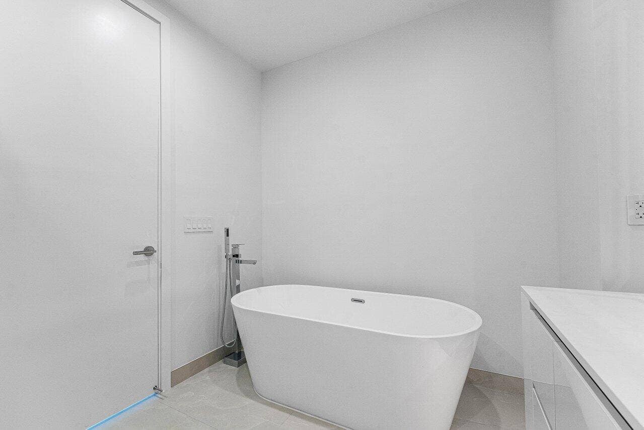 Freestanding white soaking tub with a floor-mounted chrome faucet and handheld sprayer, set against polished tile flooring