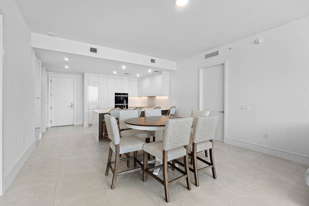 Open-concept kitchen featuring high-gloss white cabinetry, a center island with integrated seating, recessed lighting, and large-format tile flooring