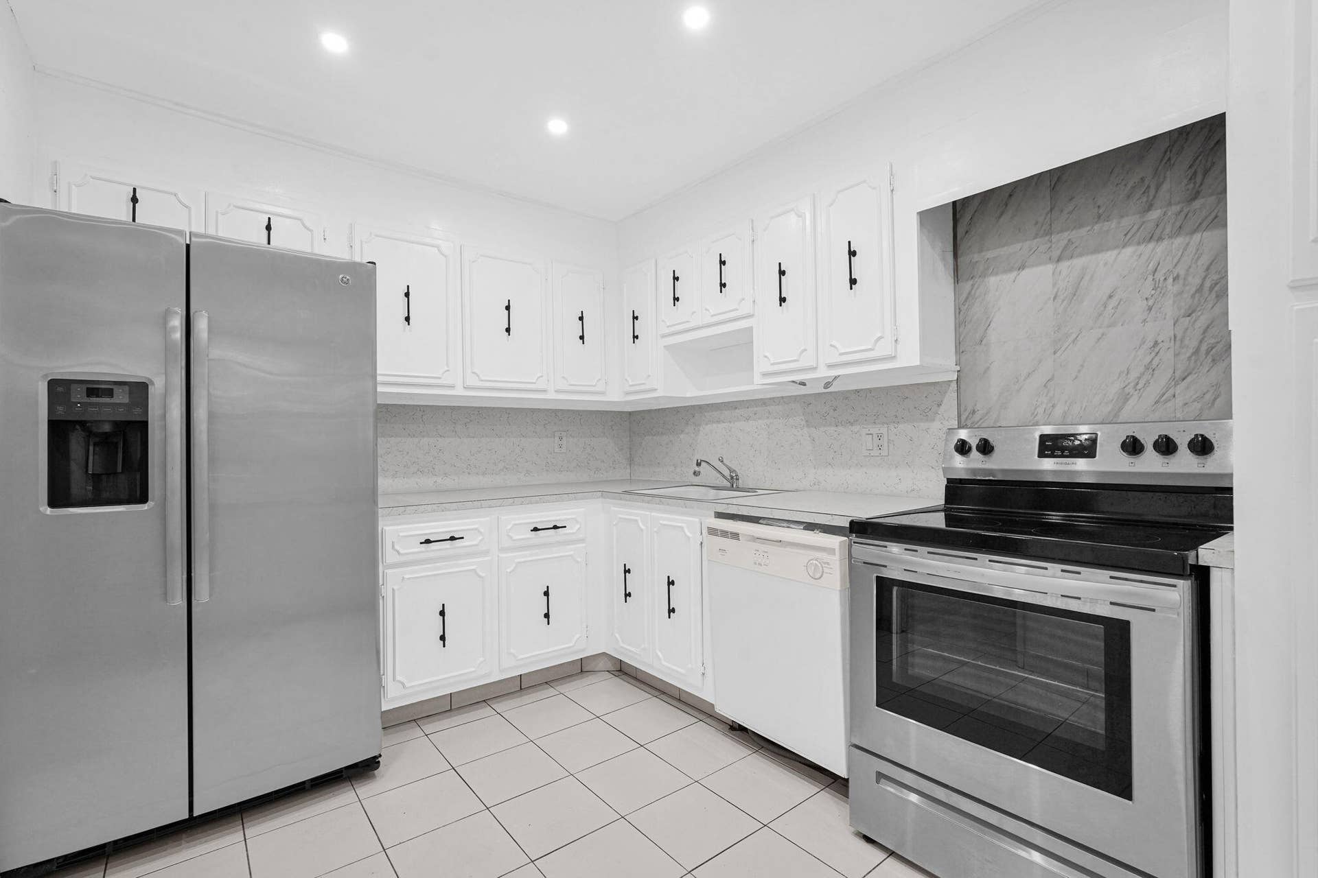 Kitchen featuring white cabinetry with matte black hardware, light-toned stone-finish countertops, stainless steel appliances, ceramic tile flooring, and recessed ceiling lighting