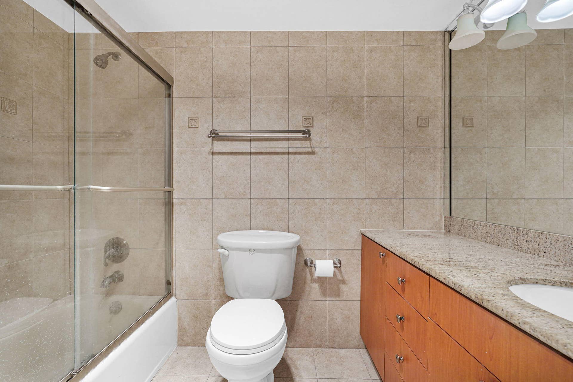 Full-length mirror, wood-veneer cabinetry with stone countertop, integrated sink, and tile-surround shower with glass enclosure
