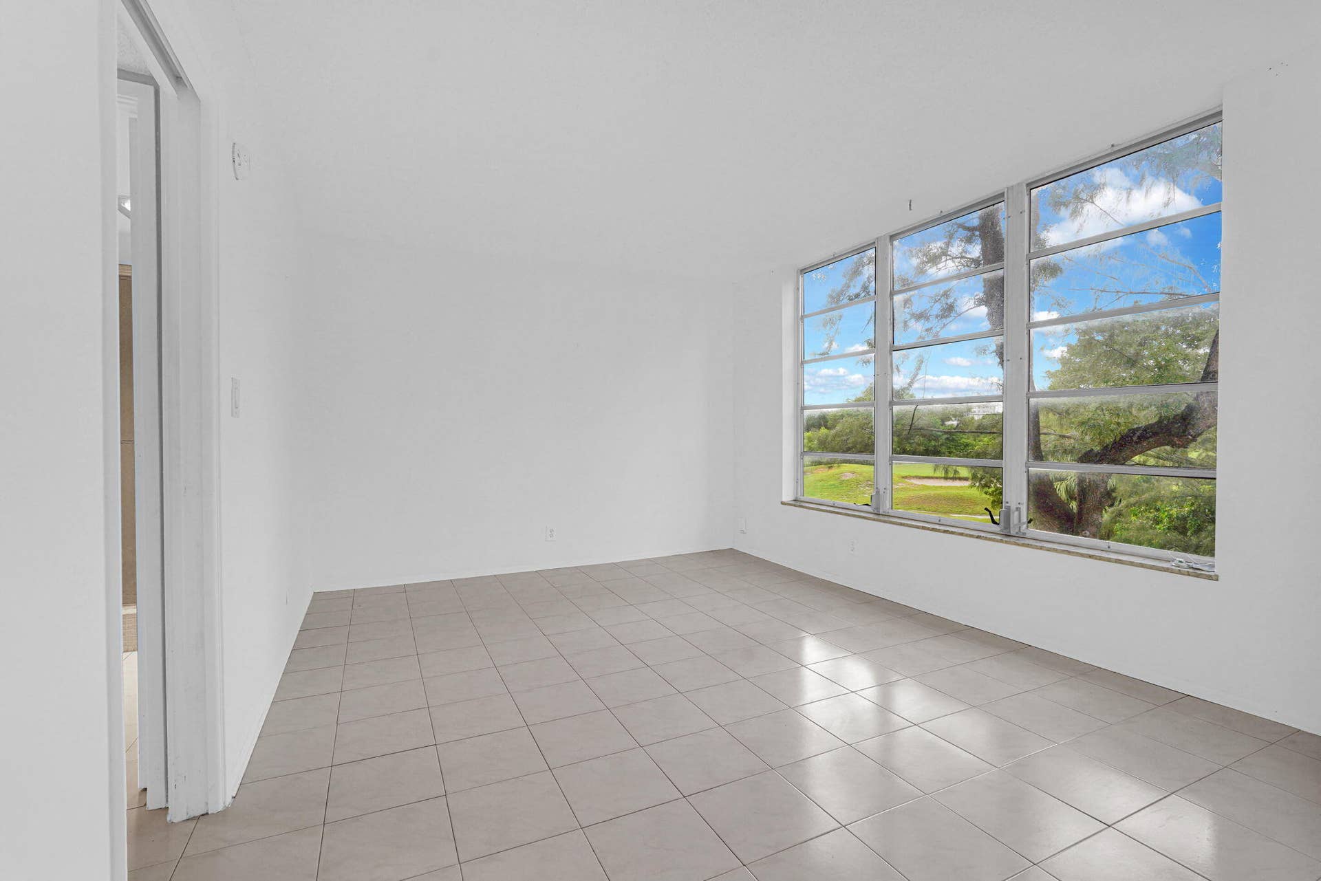 Interior space featuring large-format tile flooring, crisp white wall finishes, and a expansive multi-pane window configuration showcasing outdoor greenery