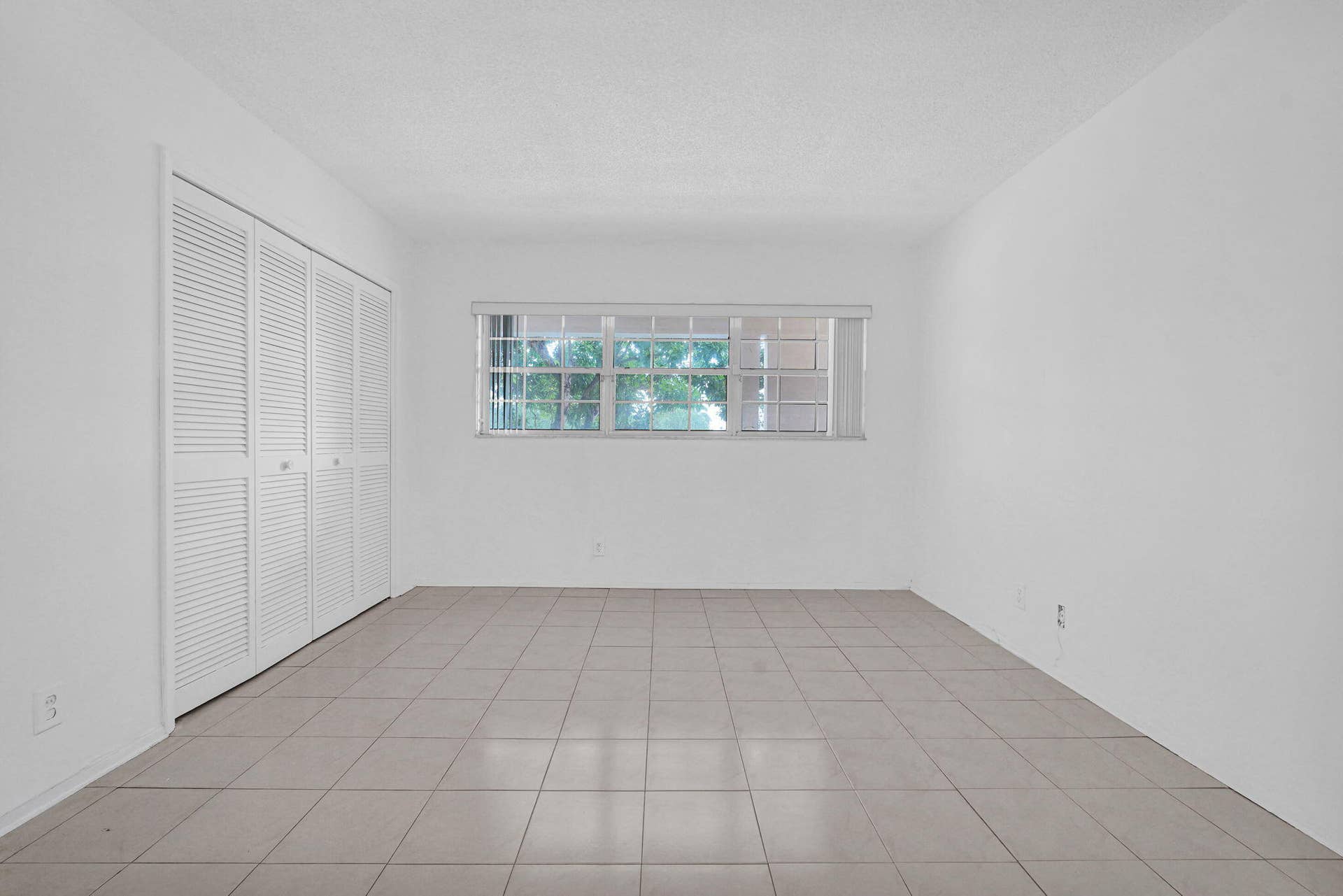 Room interior featuring neutral tile flooring, expansive wall space, and a multi-pane window with a horizontal blind