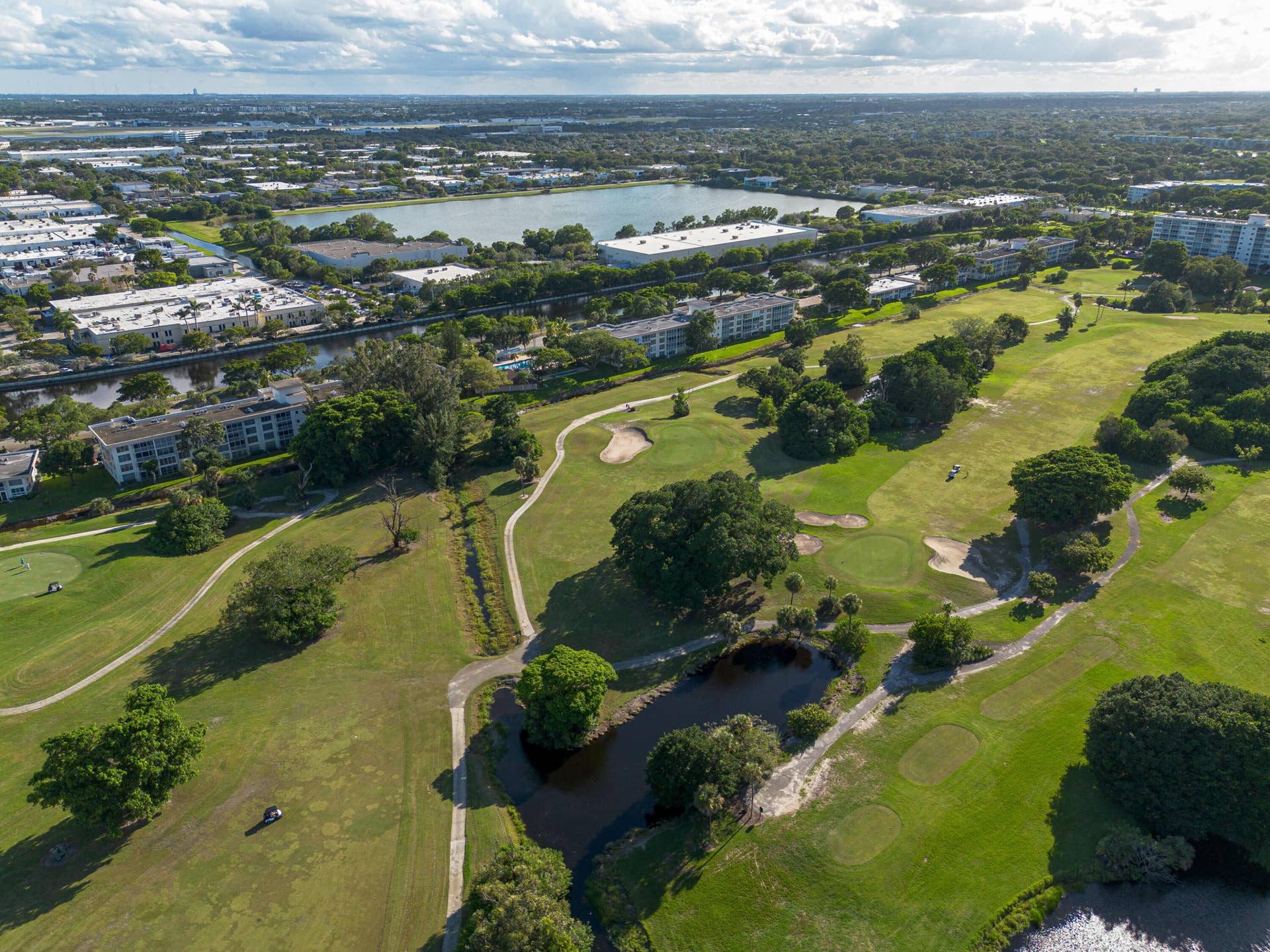 Aerial perspective of a golf course featuring manicured fairways, sand bunkers, water hazards, and mature trees