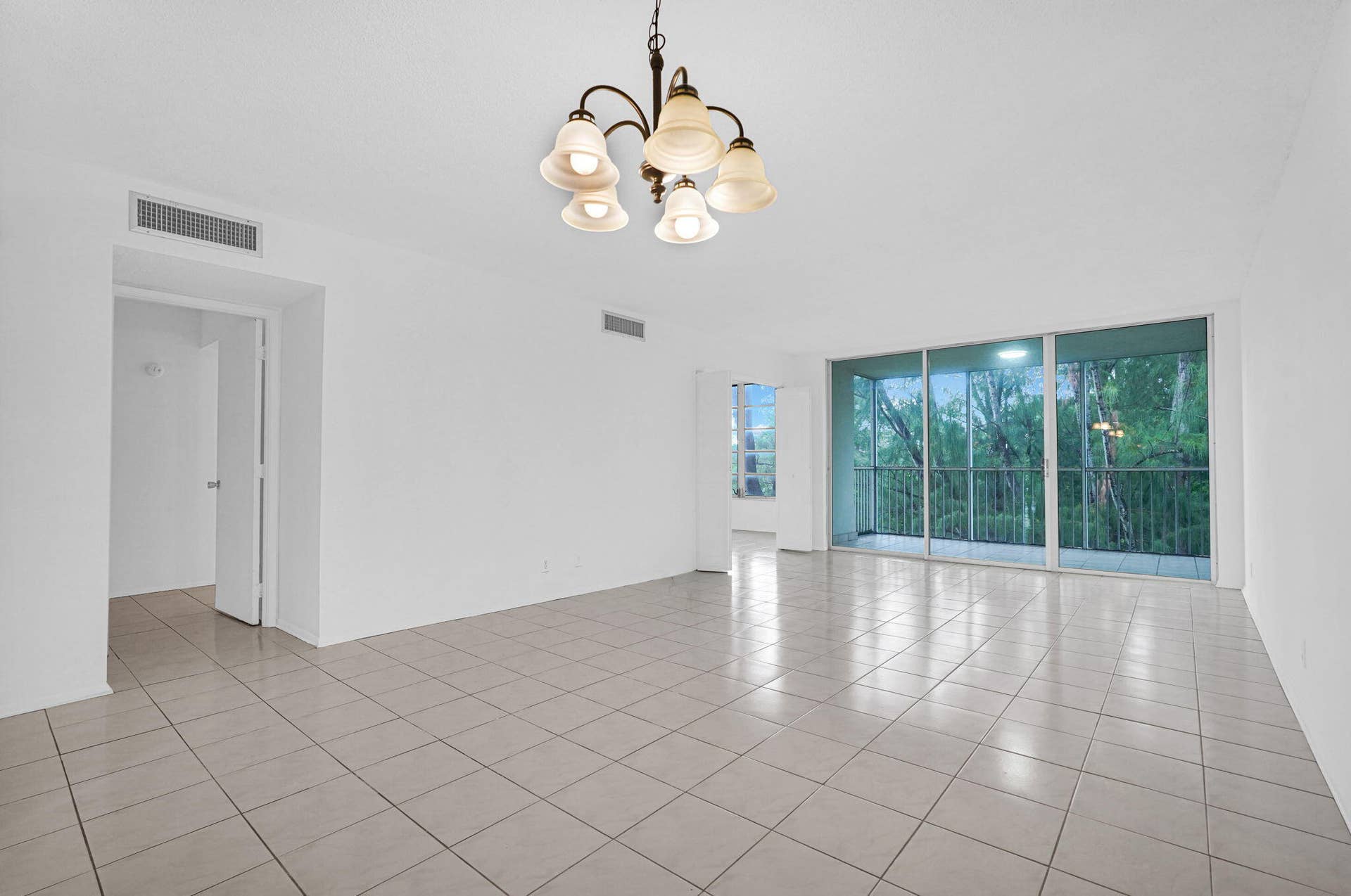 Spacious room featuring neutral ceramic tile flooring, a multi-arm chandelier with frosted glass shades, and floor-to-ceiling sliding glass doors