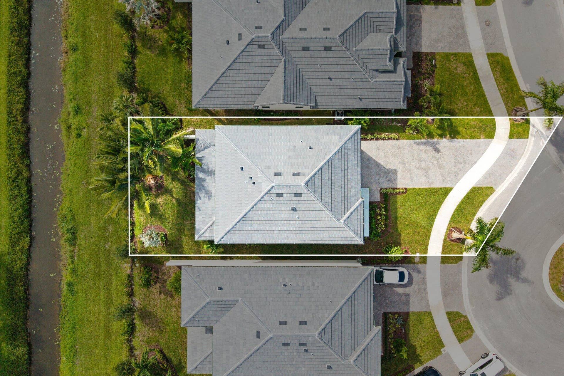 Aerial perspective of a property featuring a concrete paver driveway, hip roof construction, manicured lawn, and water frontage