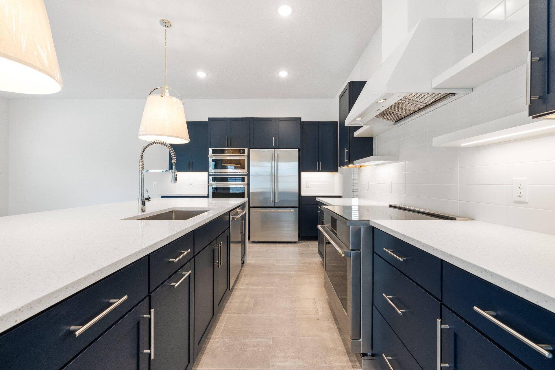Kitchen featuring dark navy cabinetry, white quartz countertops, stainless steel appliances, a tile backsplash, and oversized pendant lighting