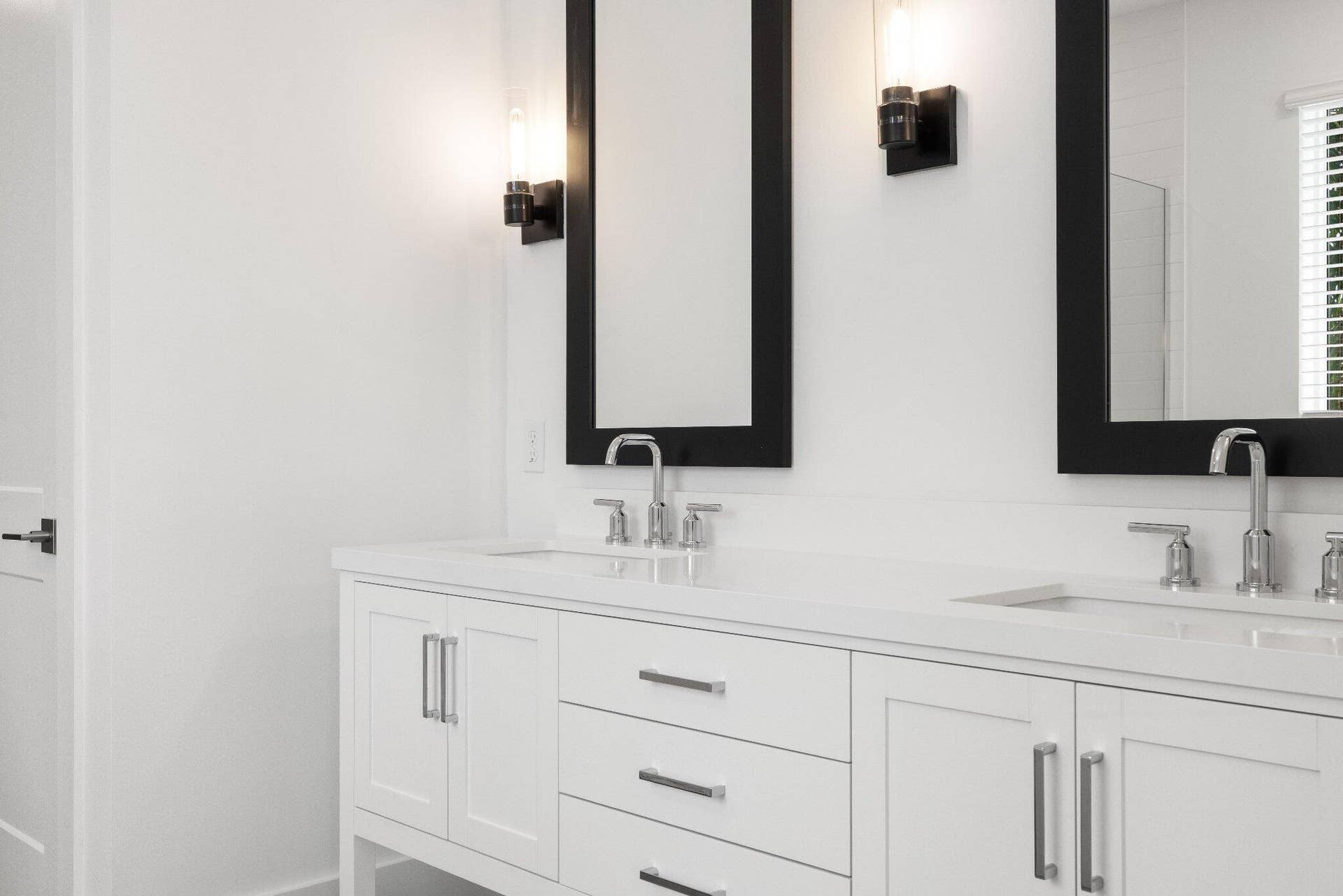 Dual-vanity cabinetry with white finish, solid surface countertop, chrome dual-handle faucets, and rectangular wall-mounted mirrors with black frames