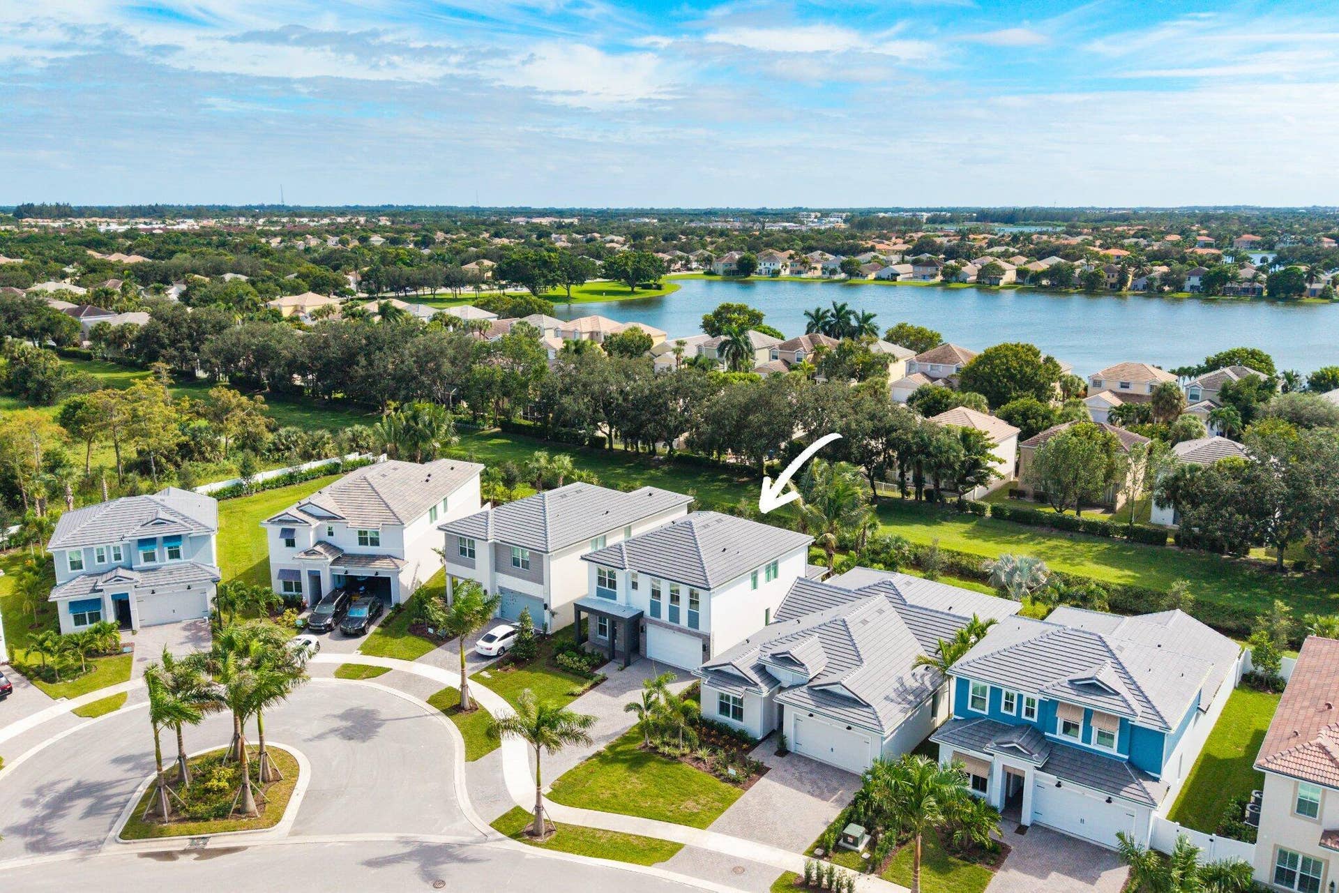 Two-story residence featuring a tile roof, light-toned exterior finish, attached two-car garage, and brick-paver driveway, situated on a lot bordering a community lake