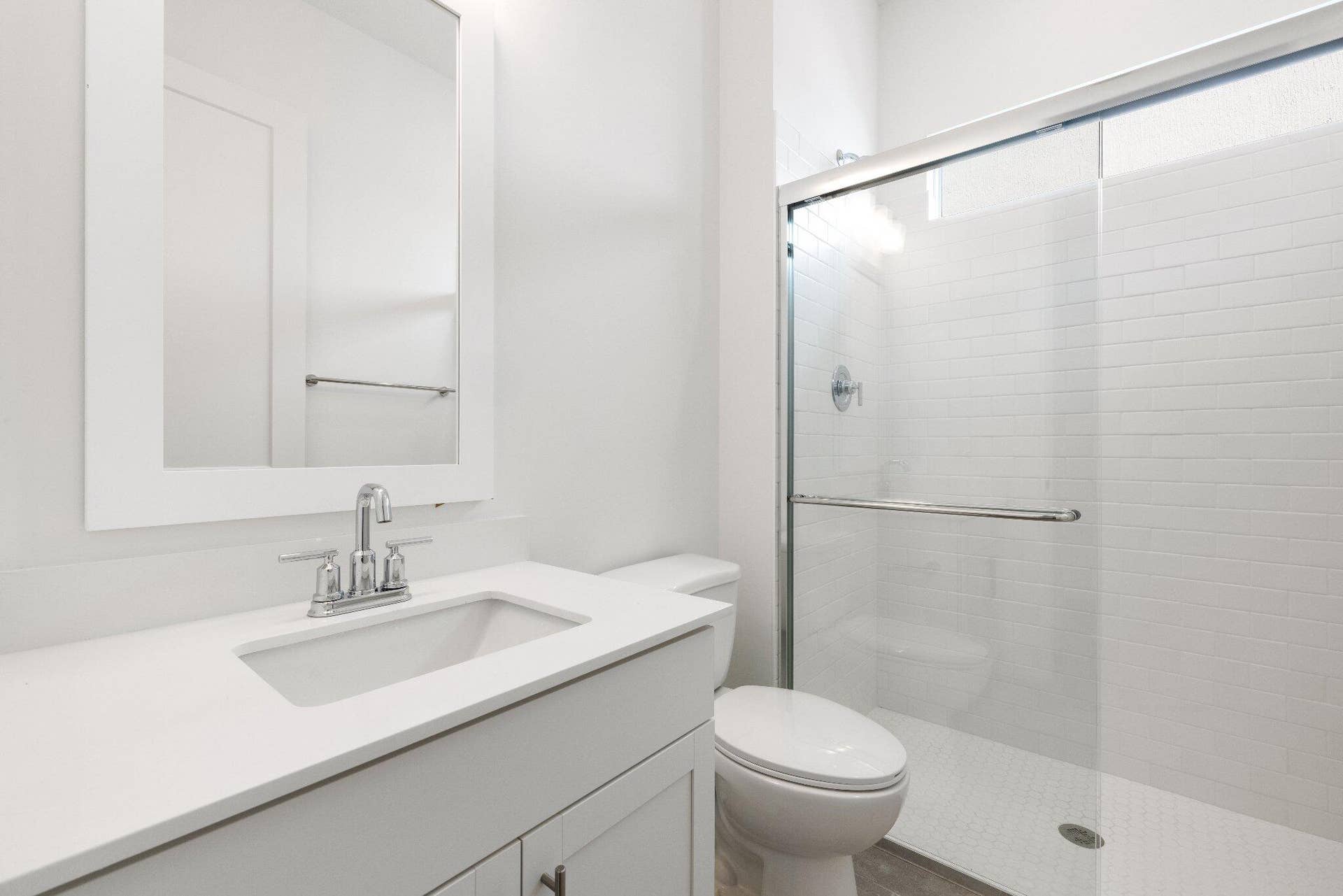 White vanity with a solid-surface countertop and undermount sink, framed rectangular wall mirror, and walk-in glass-enclosed shower featuring white subway-style wall tile