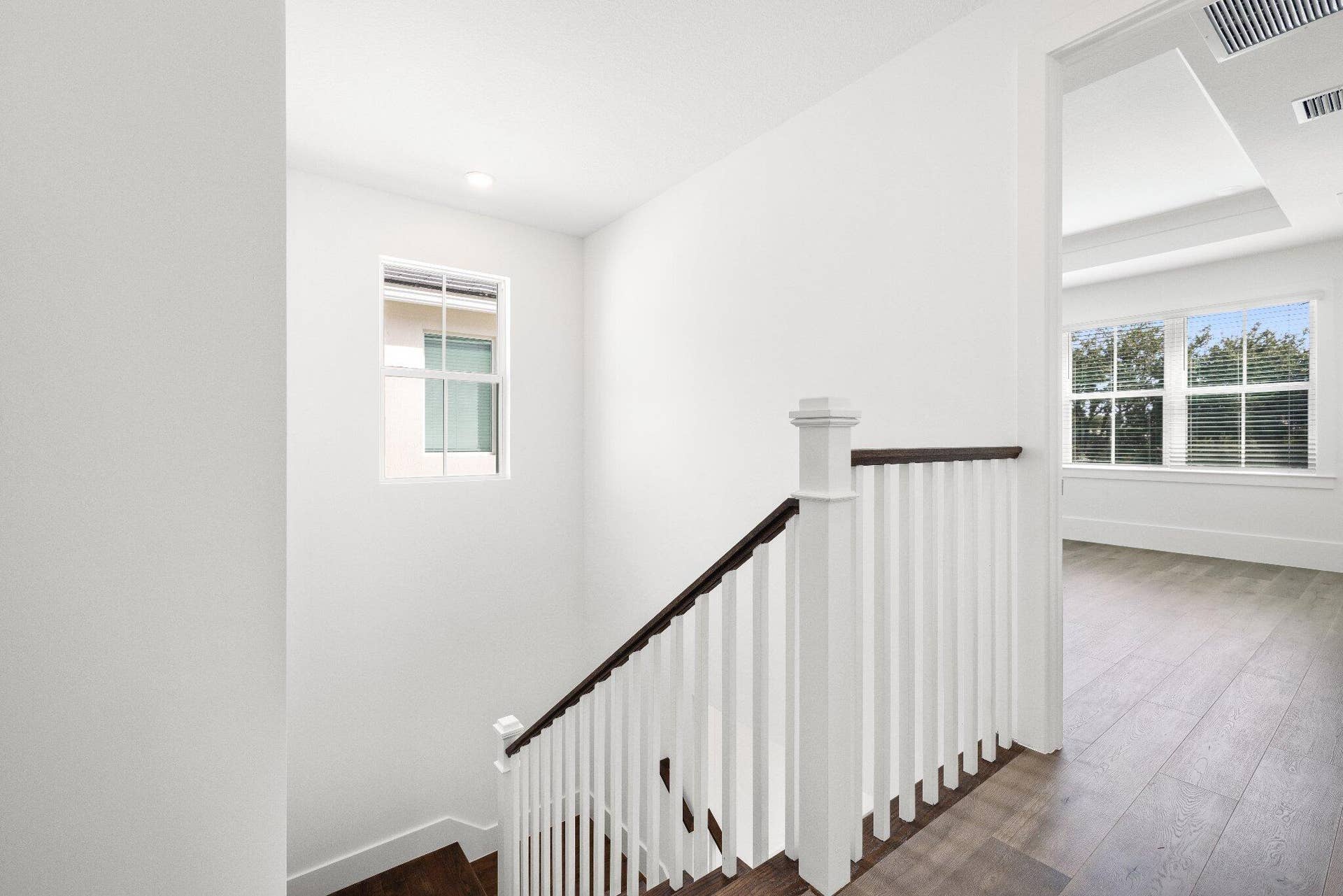 Staircase featuring dark wood-finish steps, white balusters, and a dark wood-finish handrail, complemented by wood-finish flooring and multi-pane windows