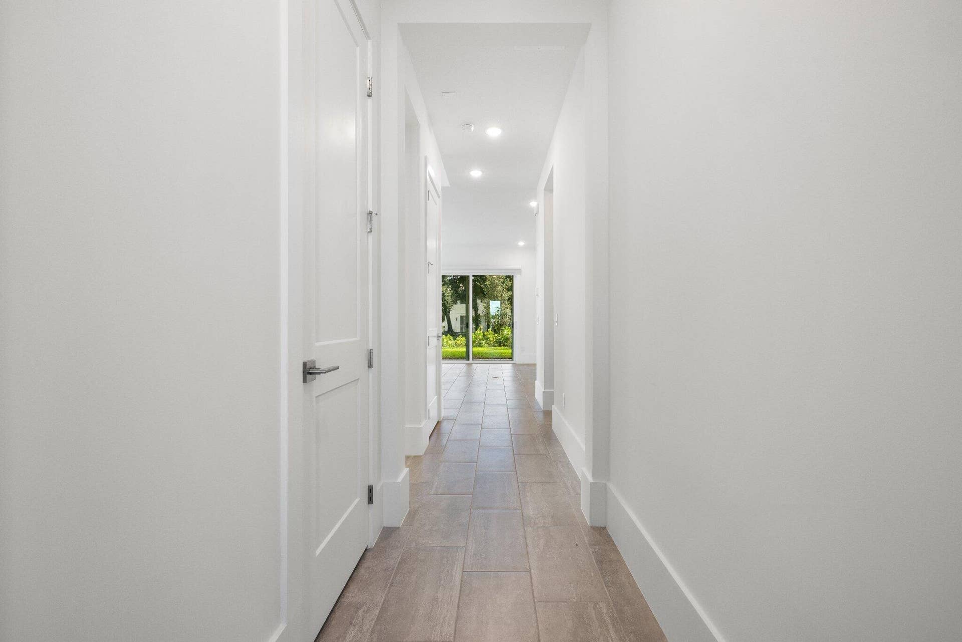 Hallway featuring wood-finish flooring, white paneled doors, recessed ceiling lighting, and sliding glass doors