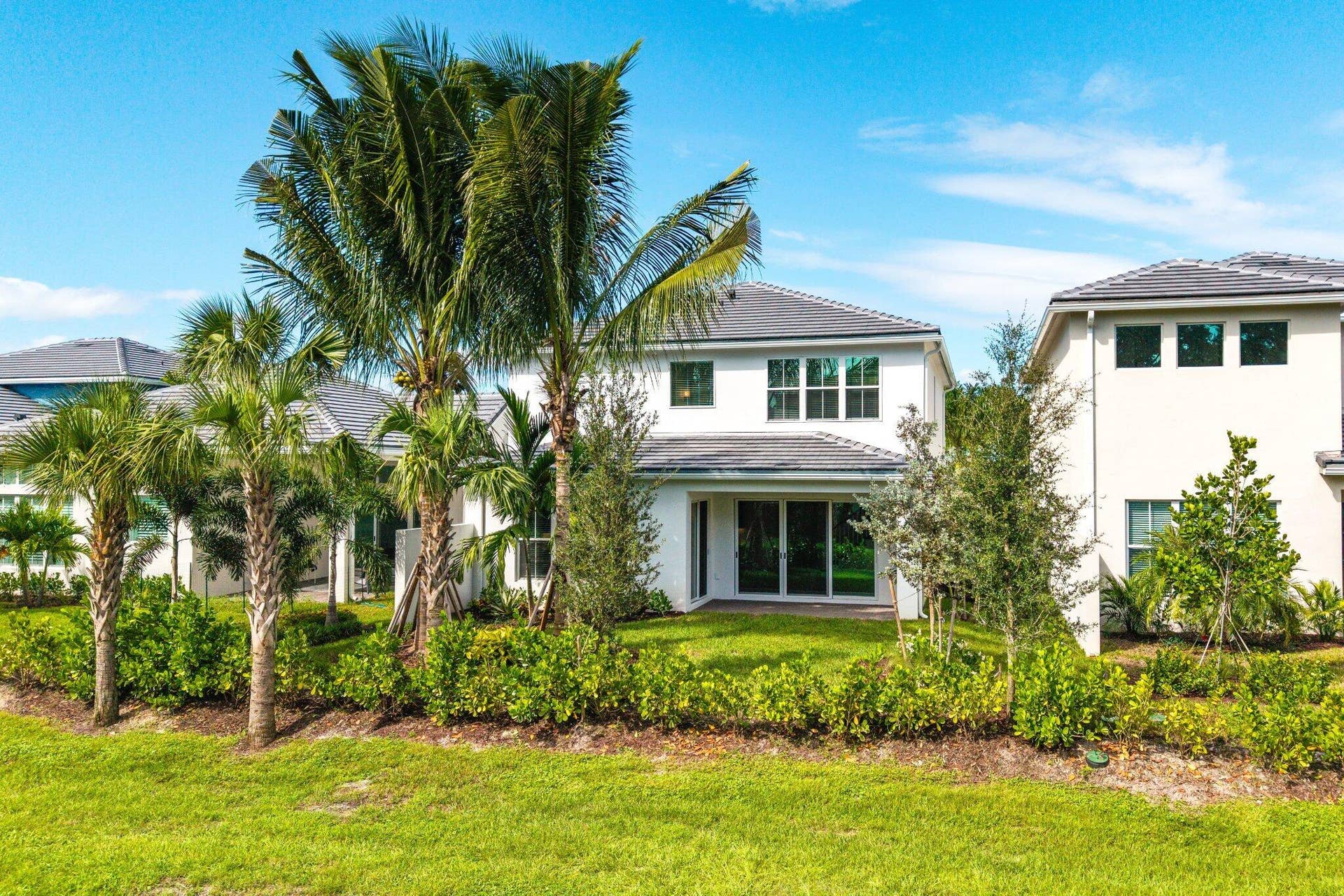 Two-story stucco exterior featuring a tile roof, multi-panel glass sliding doors, and mature palm landscaping