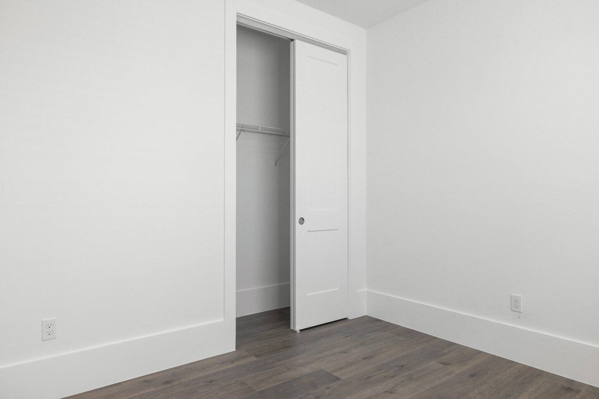 Room featuring wood-finish flooring, crisp neutral walls, and a single-panel interior door opening to a closet with built-in wire shelving