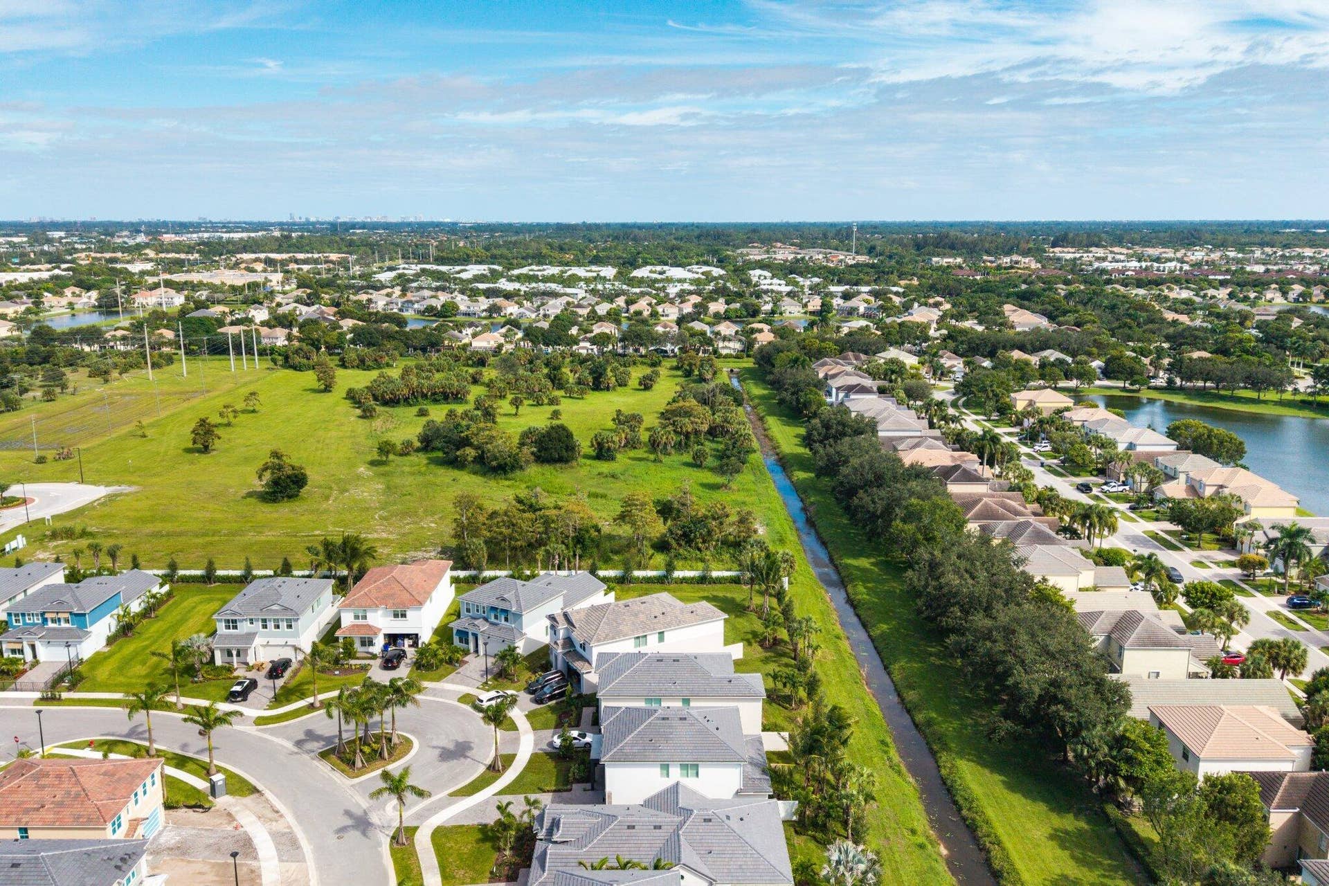 Aerial perspective showcasing a suburban residential community featuring concrete tile roofing, cul-de-sac streets, established landscaping, and bordering water features