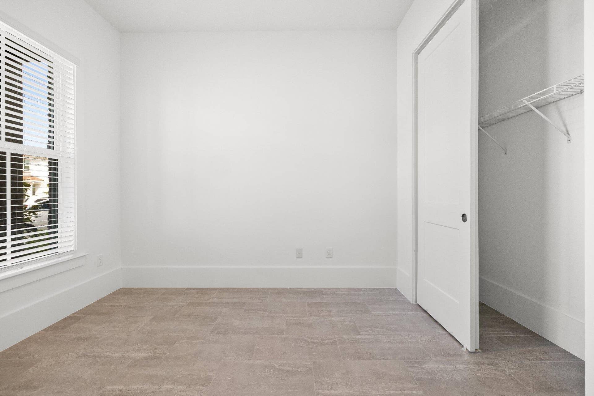 Neutral-toned tile flooring, single-pane window with installed horizontal blinds, and a built-in closet with a panel door and wire shelving
