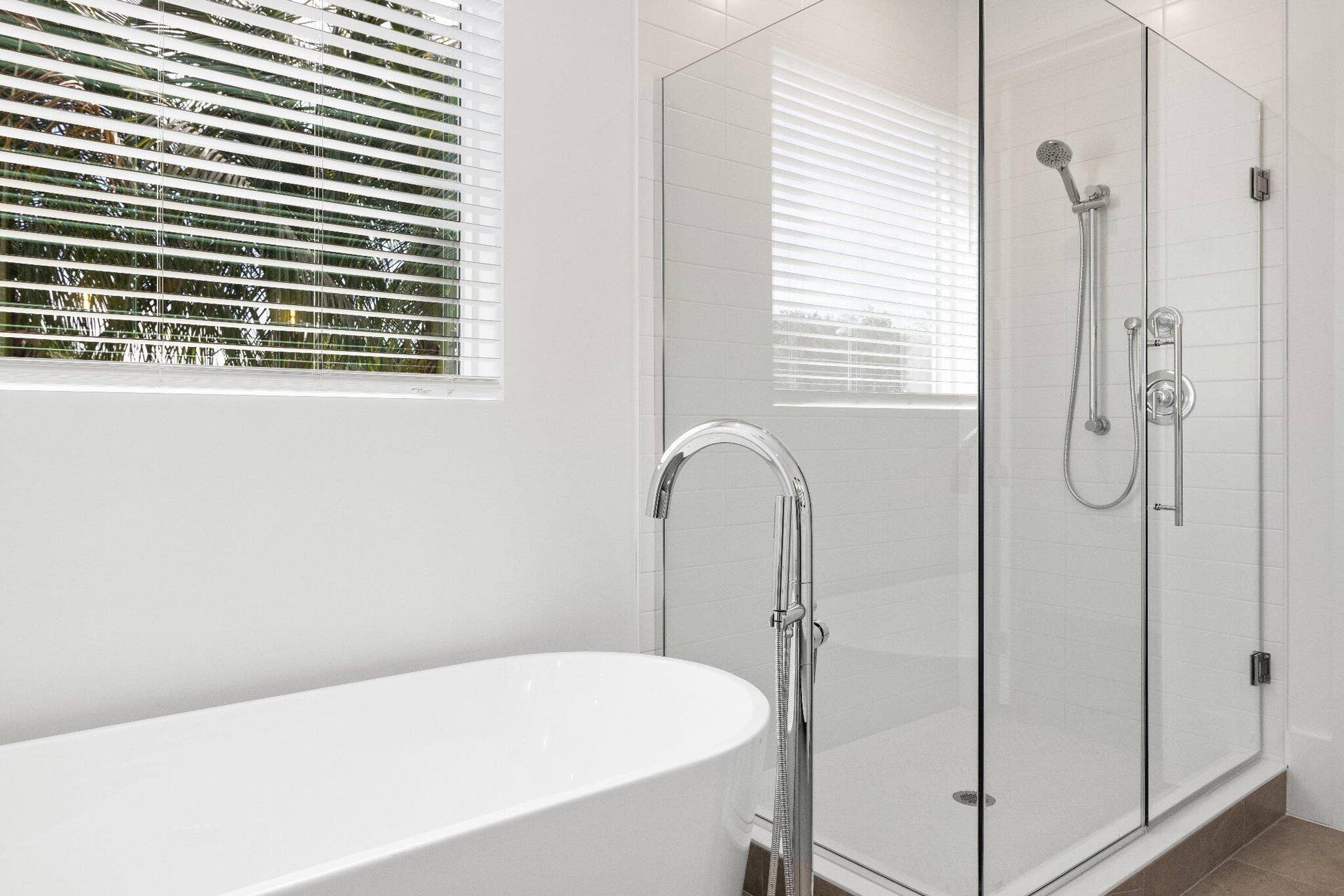 Freestanding soaking tub with a chrome floor-mounted faucet, walk-in shower with a glass enclosure, and handheld shower fixture