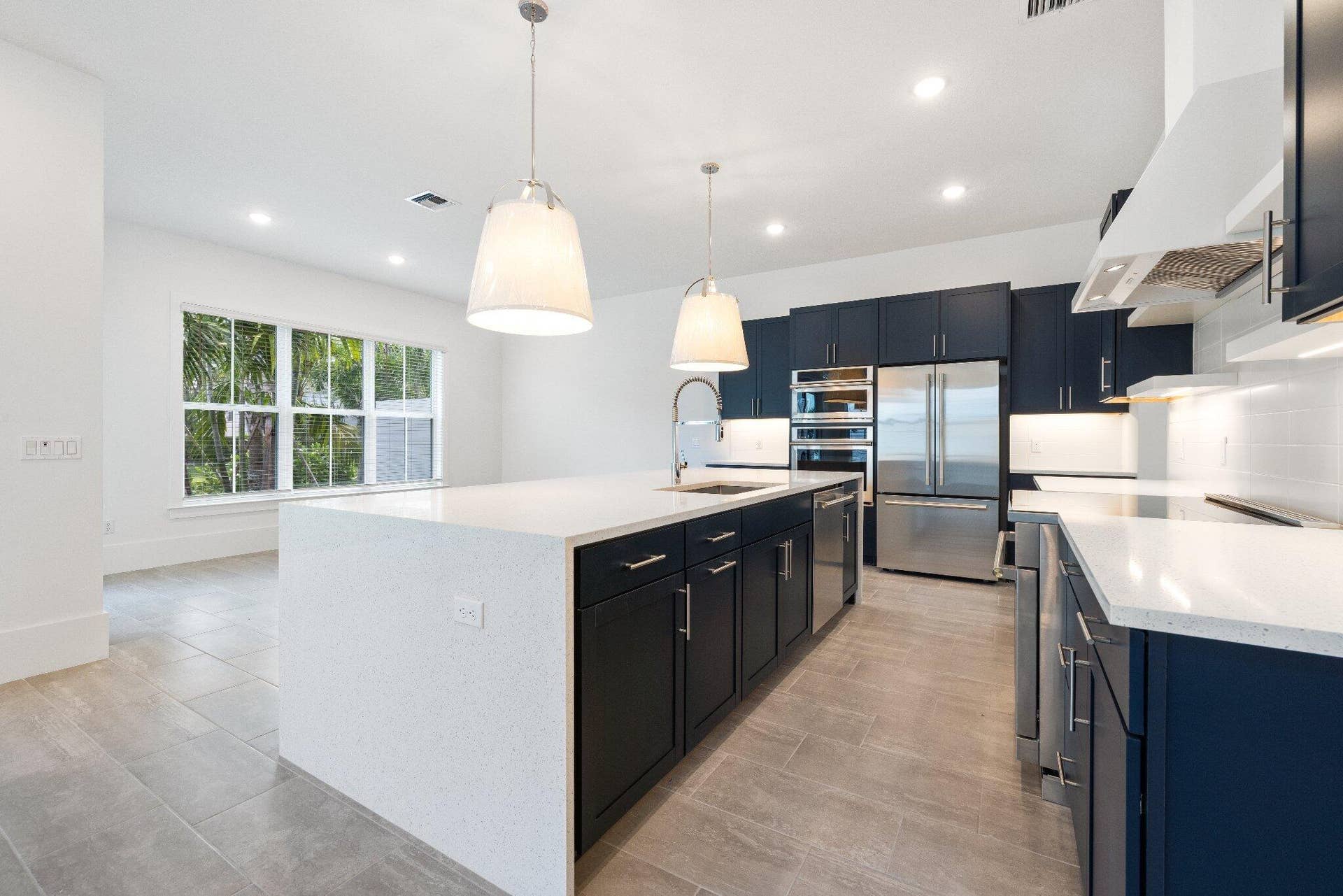 Kitchen featuring dark cabinetry, quartz countertops, a waterfall-edge center island, stainless steel built-in appliances, and tile flooring