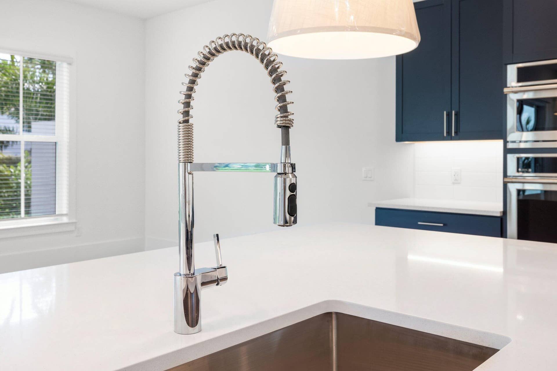 Quartz countertop with undermount stainless steel sink, professional-style high-arc spring faucet, navy blue cabinetry, and built-in wall oven