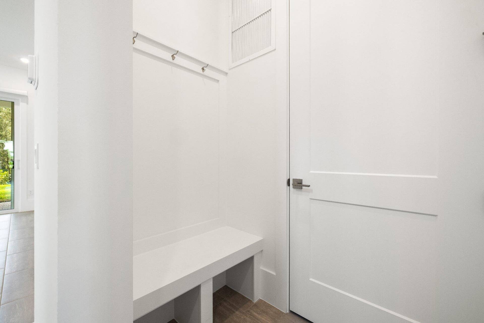 Built-in white storage bench featuring mounted wall hooks, a shaker-style interior door, and clean architectural lines