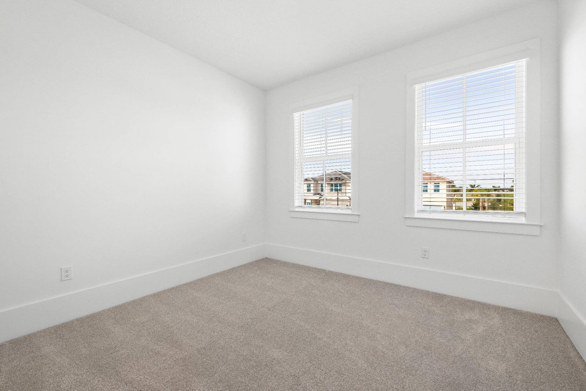Neutral interior space featuring wall-to-wall carpeting, two double-hung windows with integrated blinds, and white wall finishes