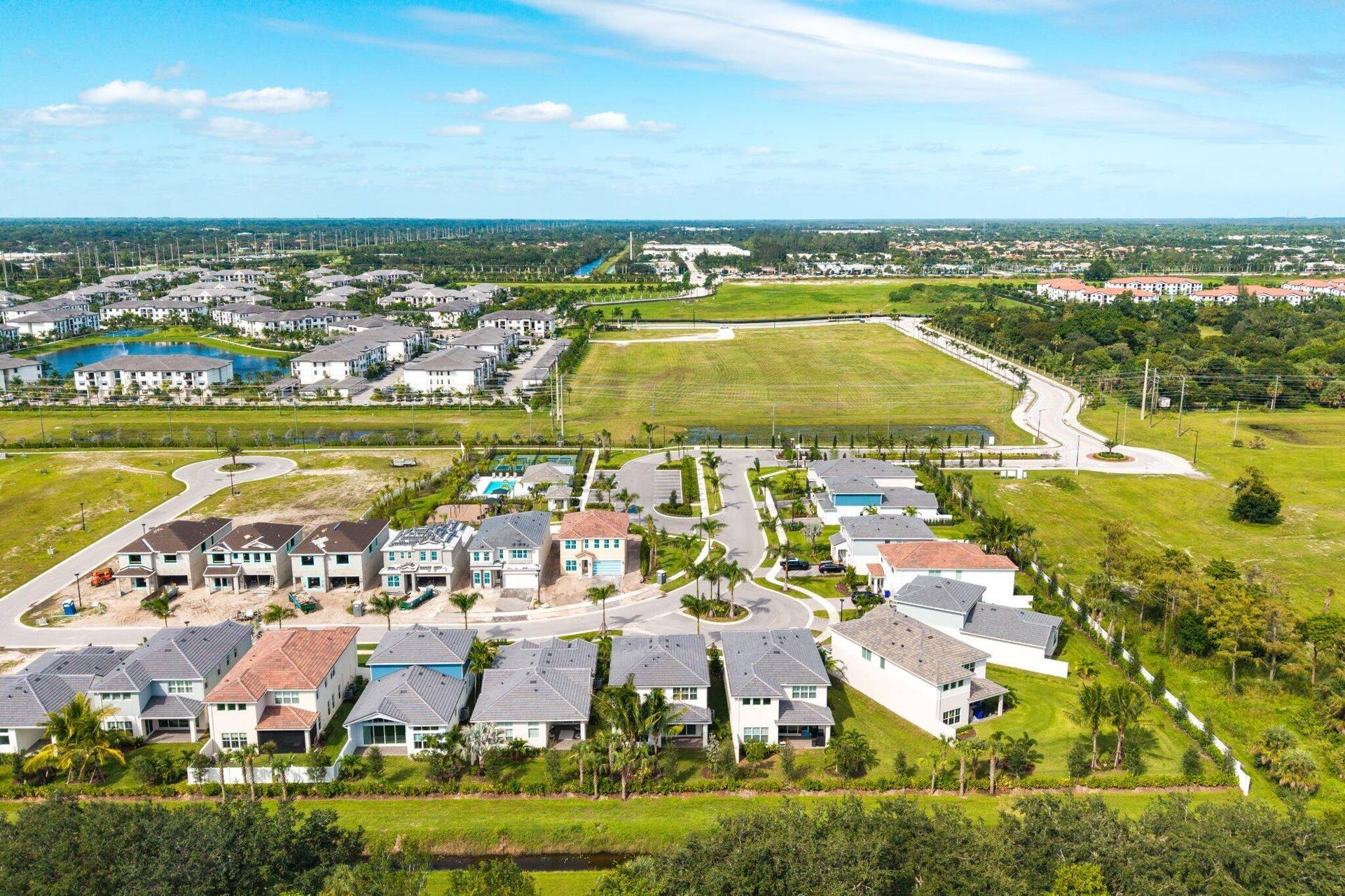Aerial perspective of a master-planned community featuring multi-story residential structures, tile roof systems, paved roadways, and integrated green spaces