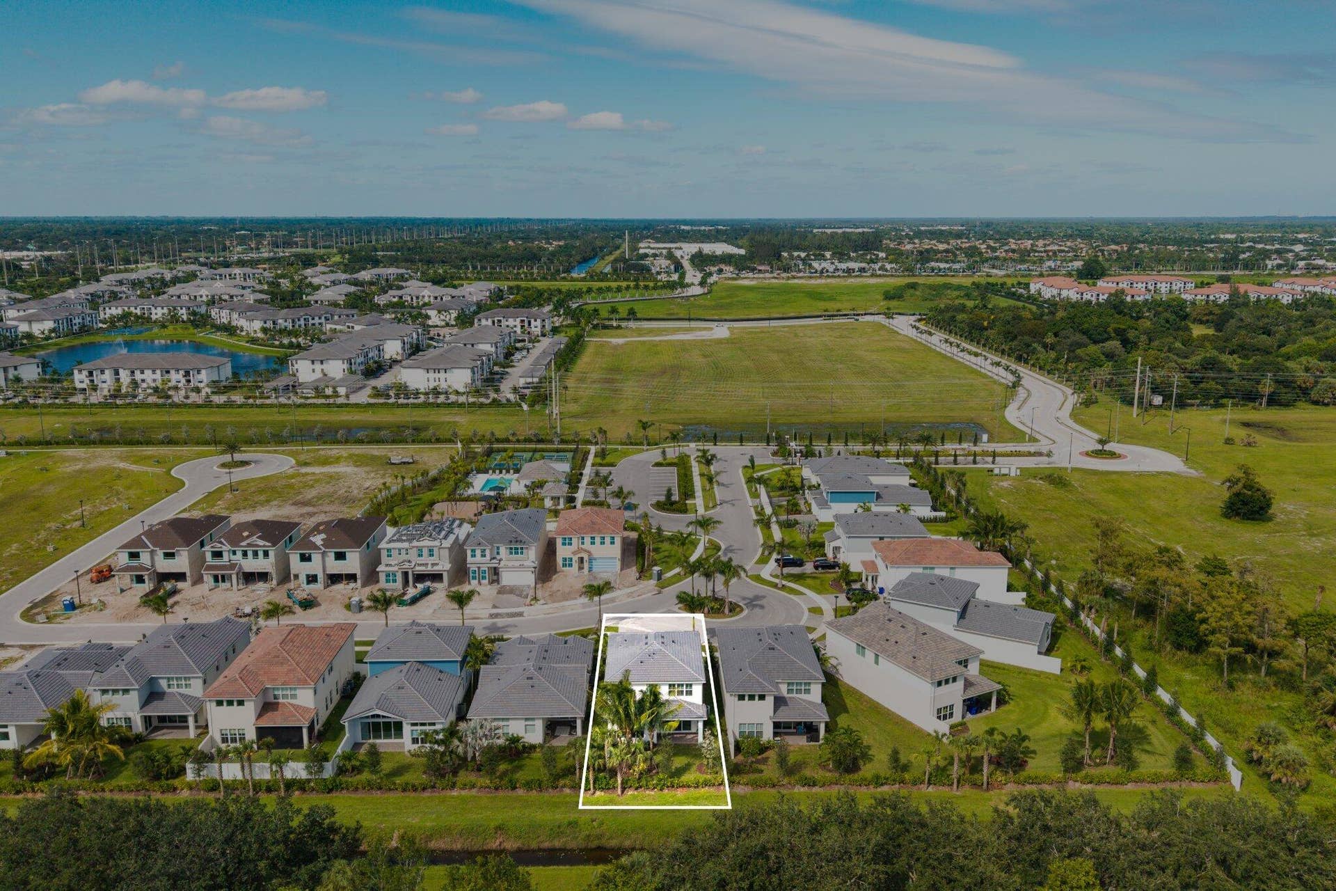 Aerial perspective of a detached residential property featuring a multi-pitched roofline, a paved driveway, and landscaping that includes mature palms