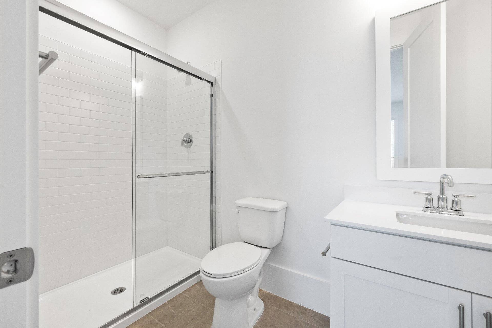 Bathroom featuring a glass-enclosed shower with white subway tile, white vanity with stone-style countertop, integrated sink, and framed wall mirror