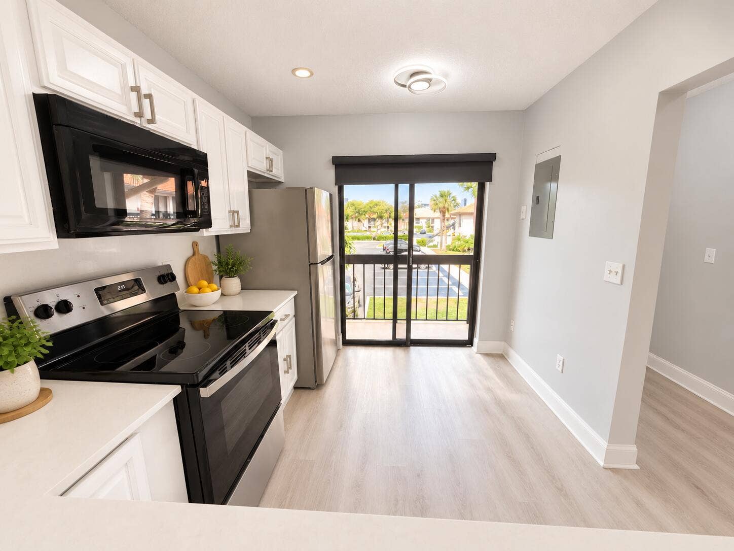 Kitchen featuring white shaker-style cabinetry, stainless steel appliances, solid-surface countertops, wood-finish flooring, and a sliding glass door with balcony access