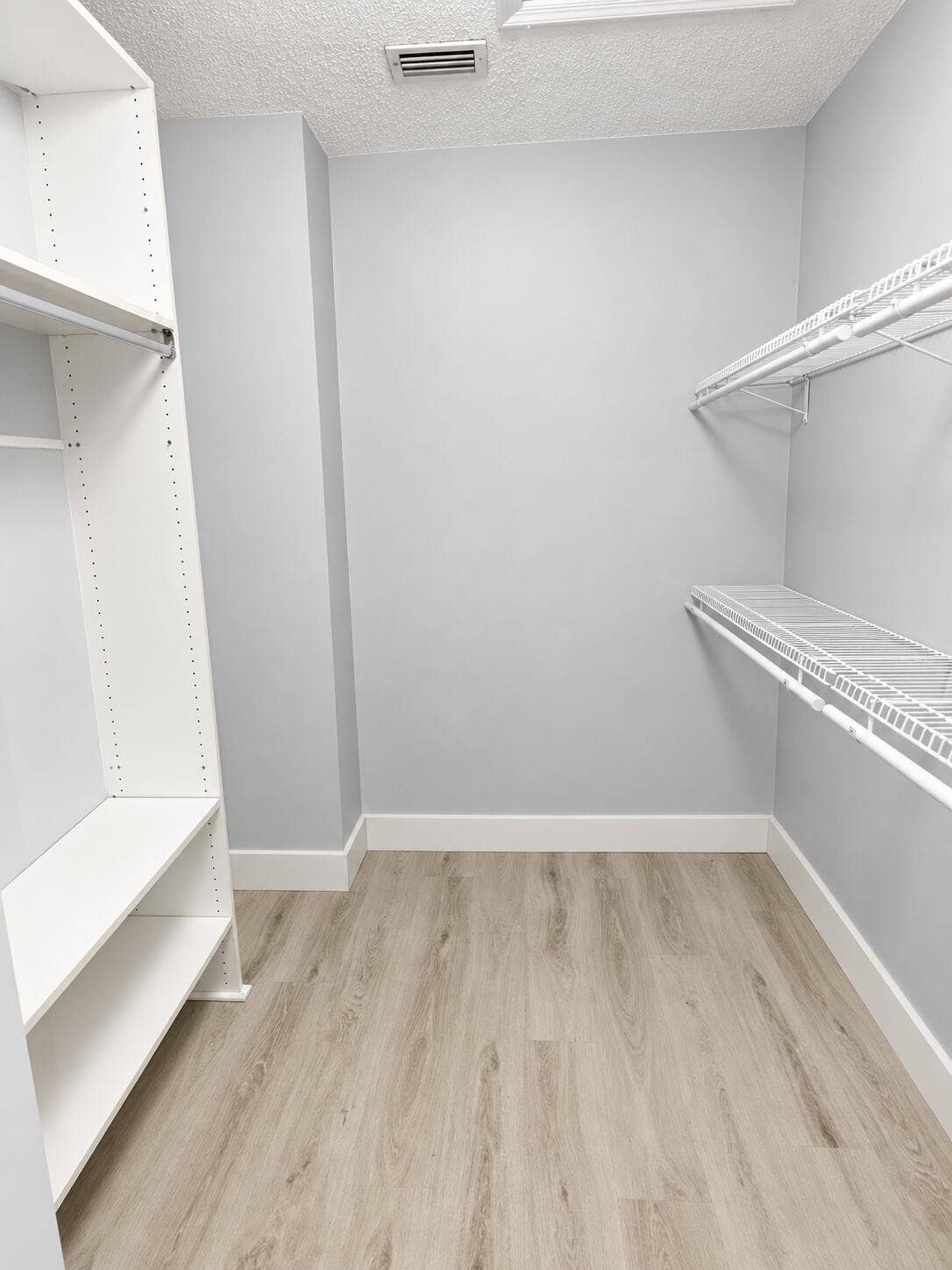 Walk-in closet featuring wood-finish flooring, white built-in shelving, and white wire rack shelving