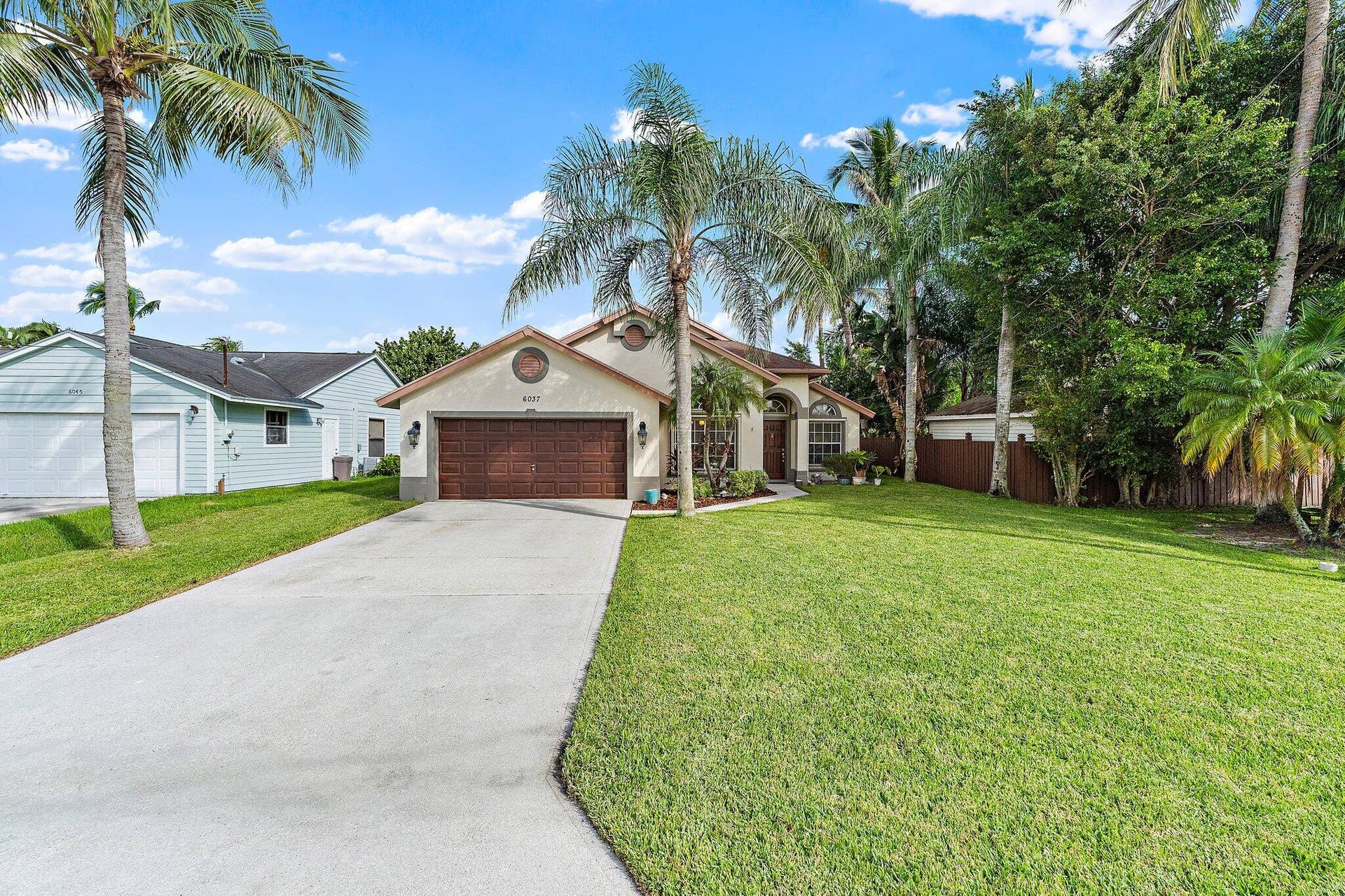 6037 Foster Street, Jupiter, FL 33458 Front of the home from the street, with the driveway and mature palms.