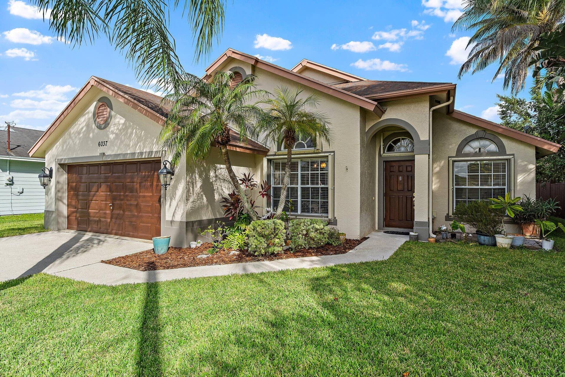 6037 Foster Street, Jupiter, FL 33458 Single-story CBS home with tropical landscaping and an attached 2-car garage.