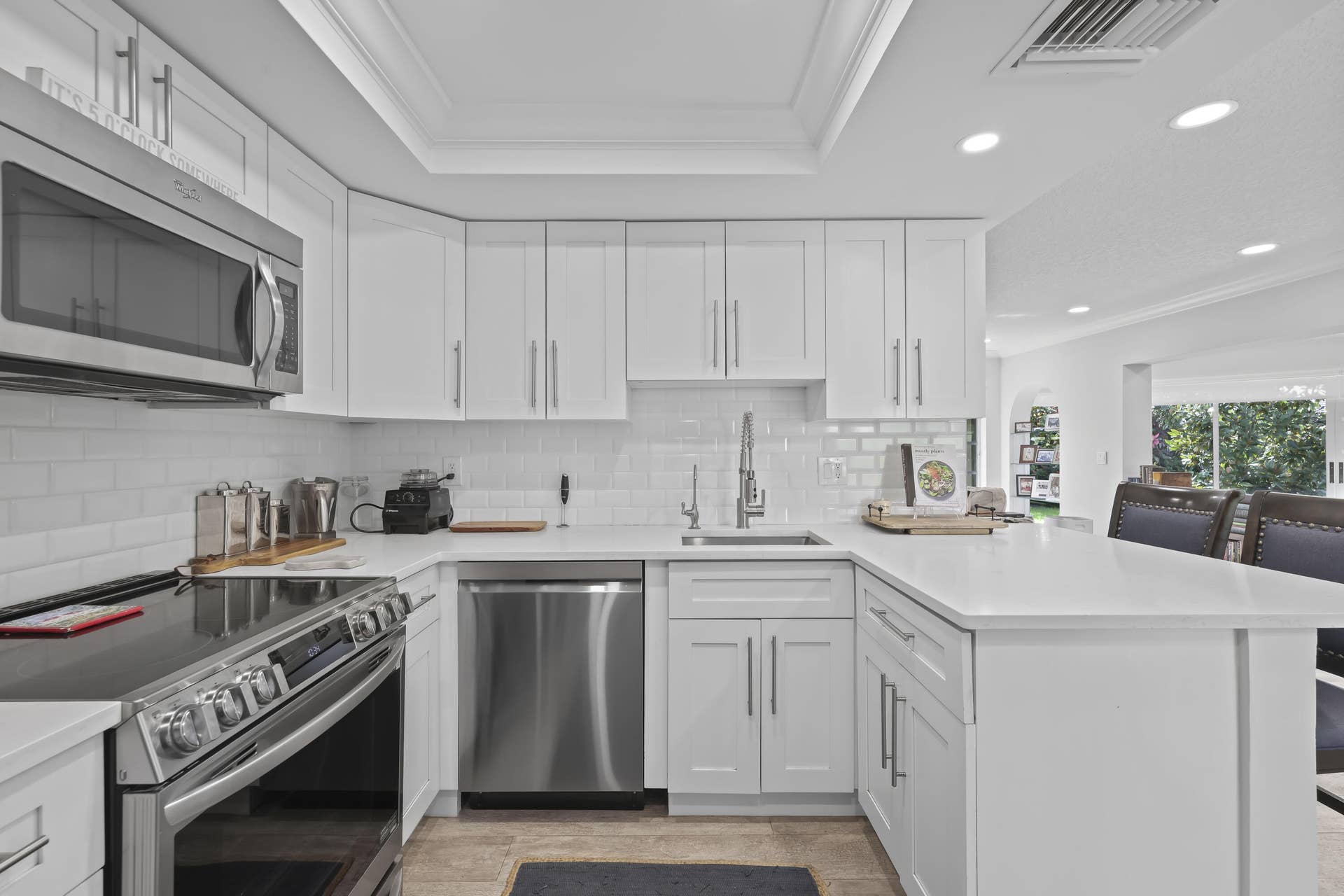 137 Clubhouse Boulevard, Atlantis, FL 33462 Kitchen featuring white Shaker-style cabinetry, stainless steel appliances, white subway tile backsplash, solid-surface countertops, and a tray ceiling with recessed lighting