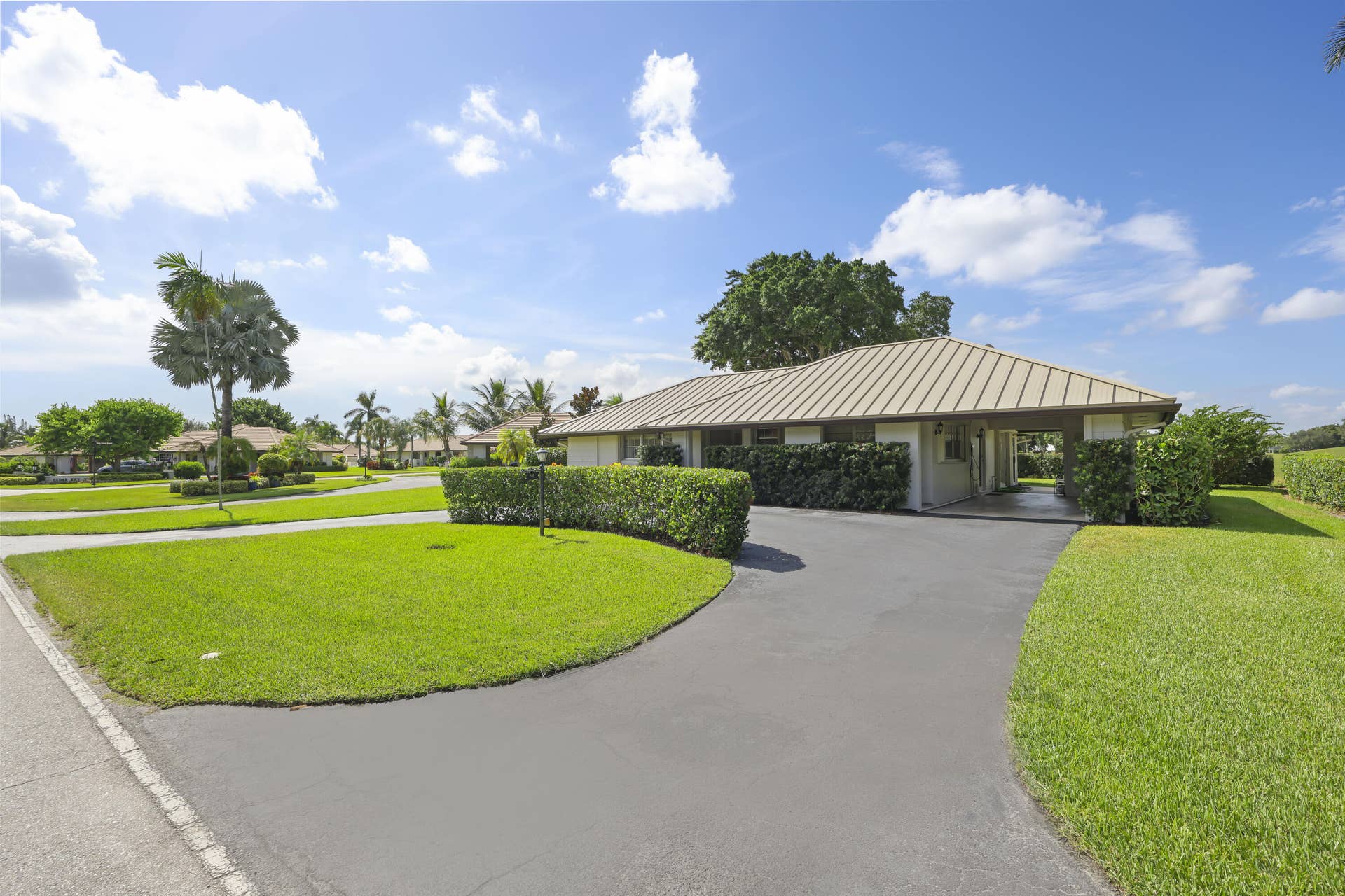 137 Clubhouse Boulevard, Atlantis, FL 33462 Single-story residence featuring a metal roof, attached carport, asphalt driveway, and manicured landscaping