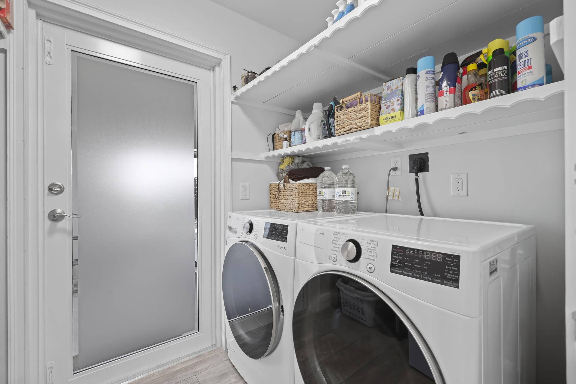 137 Clubhouse Boulevard, Atlantis, FL 33462 Laundry room featuring dual scalloped-edge wood shelves, an exterior door with frosted glass inlay, and white cabinetry finish