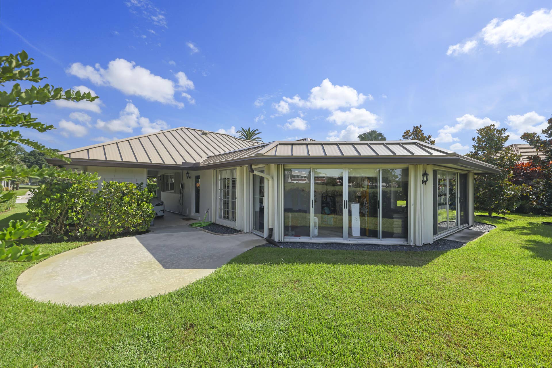 137 Clubhouse Boulevard, Atlantis, FL 33462 Single-story exterior featuring a metal roof, sliding glass wall panels, a concrete patio, and a grass lawn