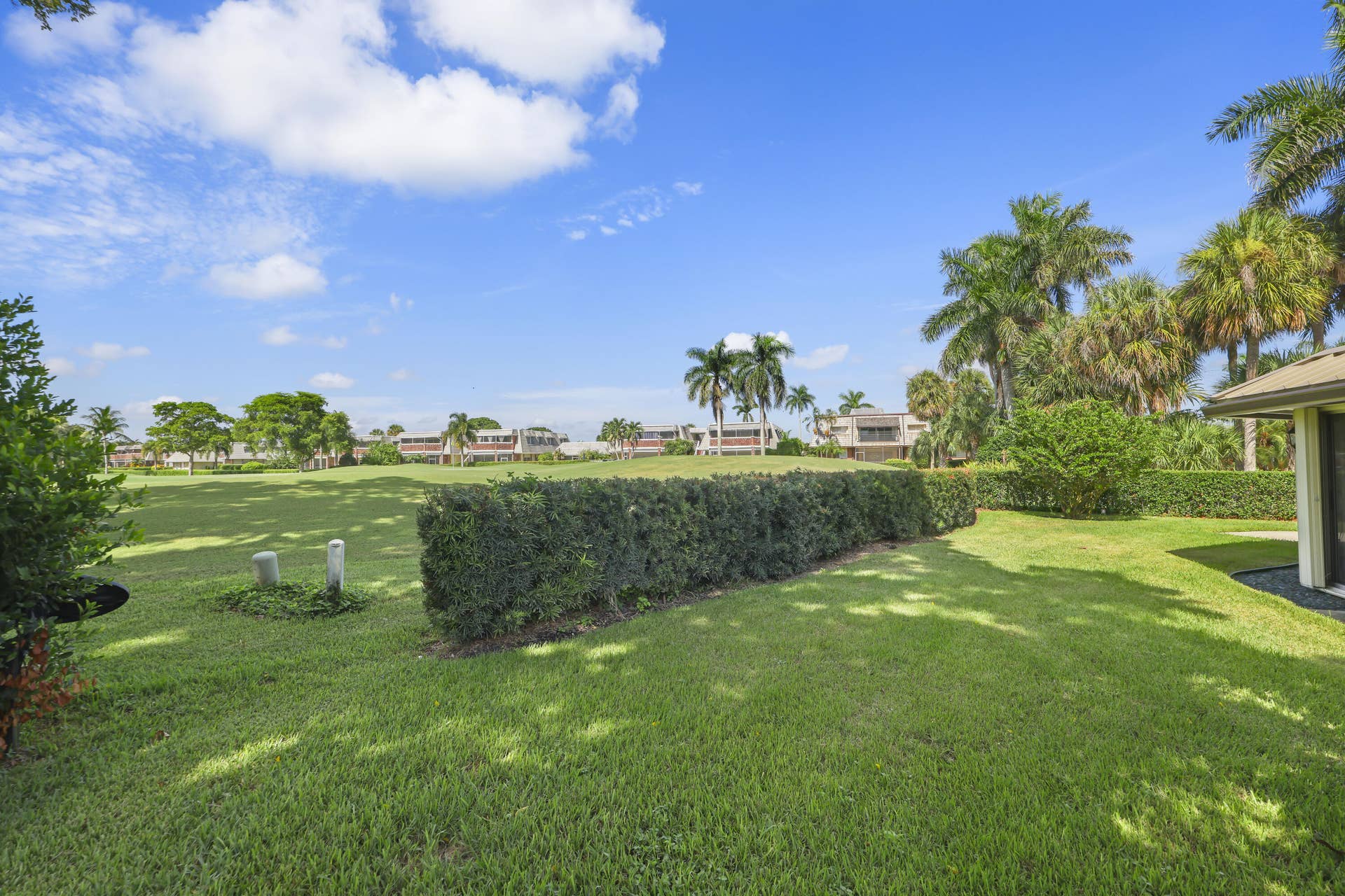 137 Clubhouse Boulevard, Atlantis, FL 33462 Expansive grassy lawn featuring manicured hedging, mature palm trees, and wide-open green space