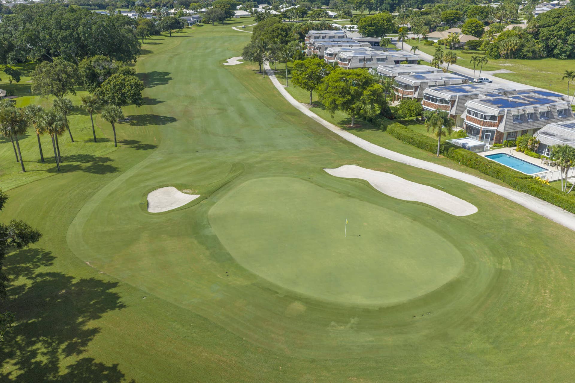 137 Clubhouse Boulevard, Atlantis, FL 33462 Aerial perspective of a golf course featuring manicured putting greens, sand bunkers, mature palm trees, and residential properties with exterior swimming pools
