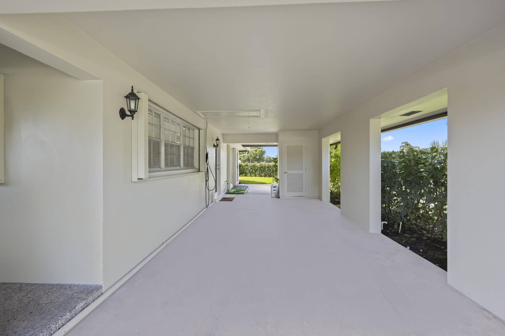 137 Clubhouse Boulevard, Atlantis, FL 33462 Covered carport featuring a concrete floor, exterior wall-mounted carriage lights, multi-pane window, and integrated storage door
