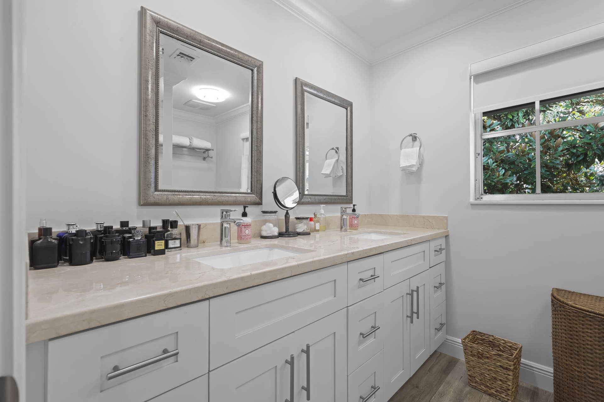 137 Clubhouse Boulevard, Atlantis, FL 33462 Double vanity featuring a light-toned stone countertop, dual undermount sinks, custom white cabinetry with brushed nickel hardware, and framed mirrors