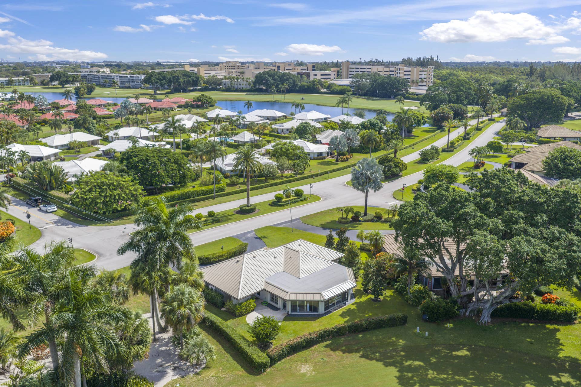 137 Clubhouse Boulevard, Atlantis, FL 33462 Aerial perspective featuring a single-story residence with a metal roof, situated on a landscaped lot with mature palm trees and expansive lawns