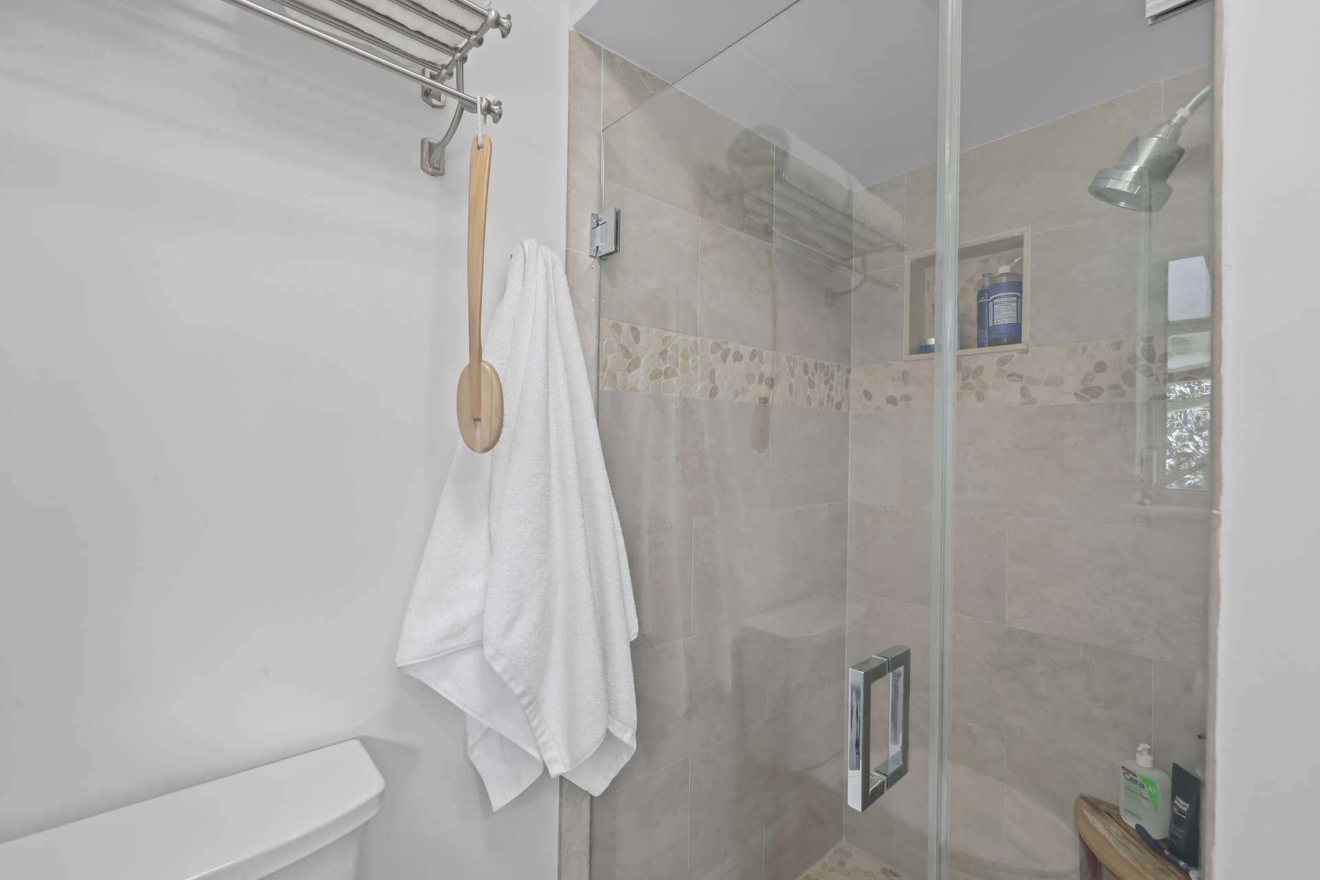 137 Clubhouse Boulevard, Atlantis, FL 33462 Shower featuring neutral stone-finish tile surround with a decorative mosaic inlay, a glass door enclosure, a built-in recessed shelf, and a polished metal shower head